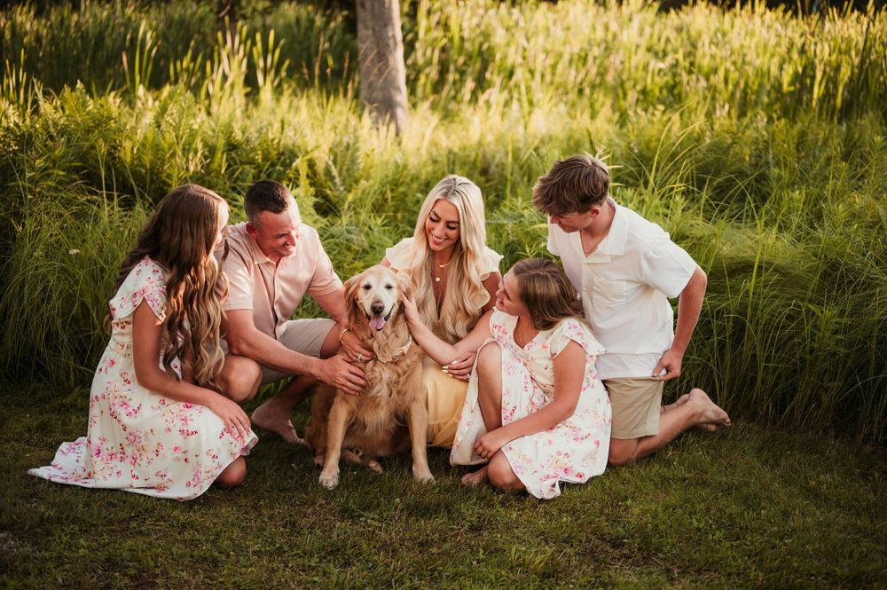 A family sits together on grass with their golden retriever during a warm sunset photoshoot.