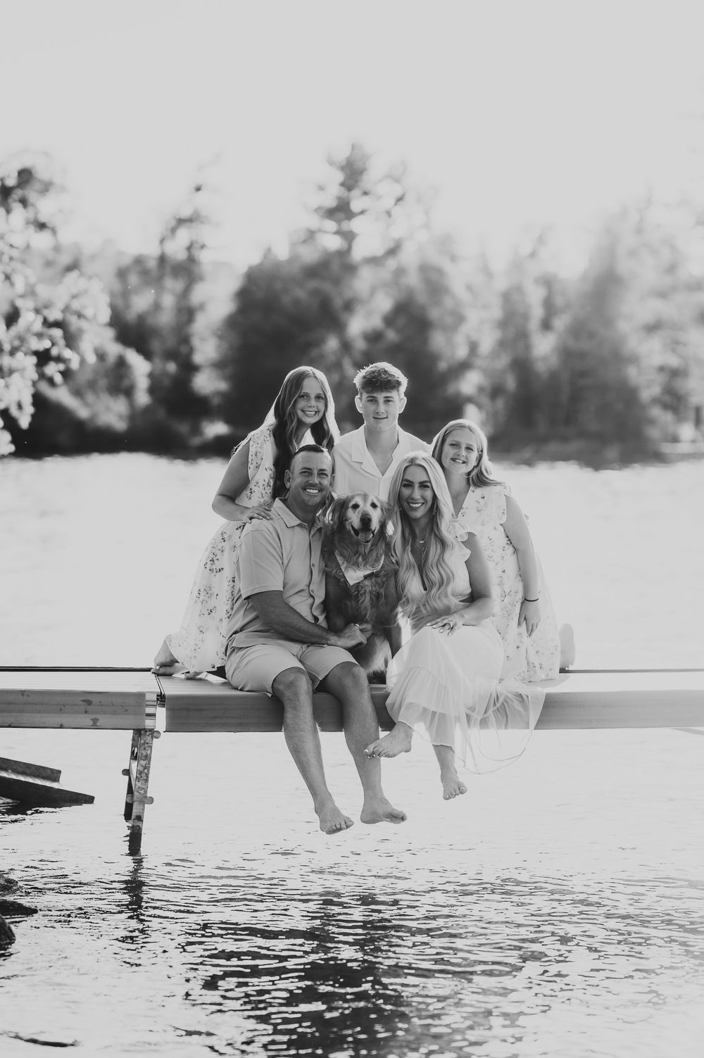 Friends sitting on a dock over a lake laughing and dipping feet in the water in black and white series.