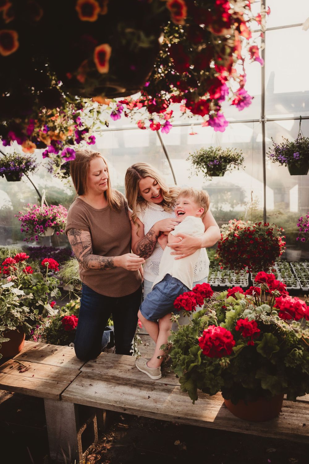 A joyful moment in a greenhouse filled with vibrant pink and red flowers as a family shares laughter together.