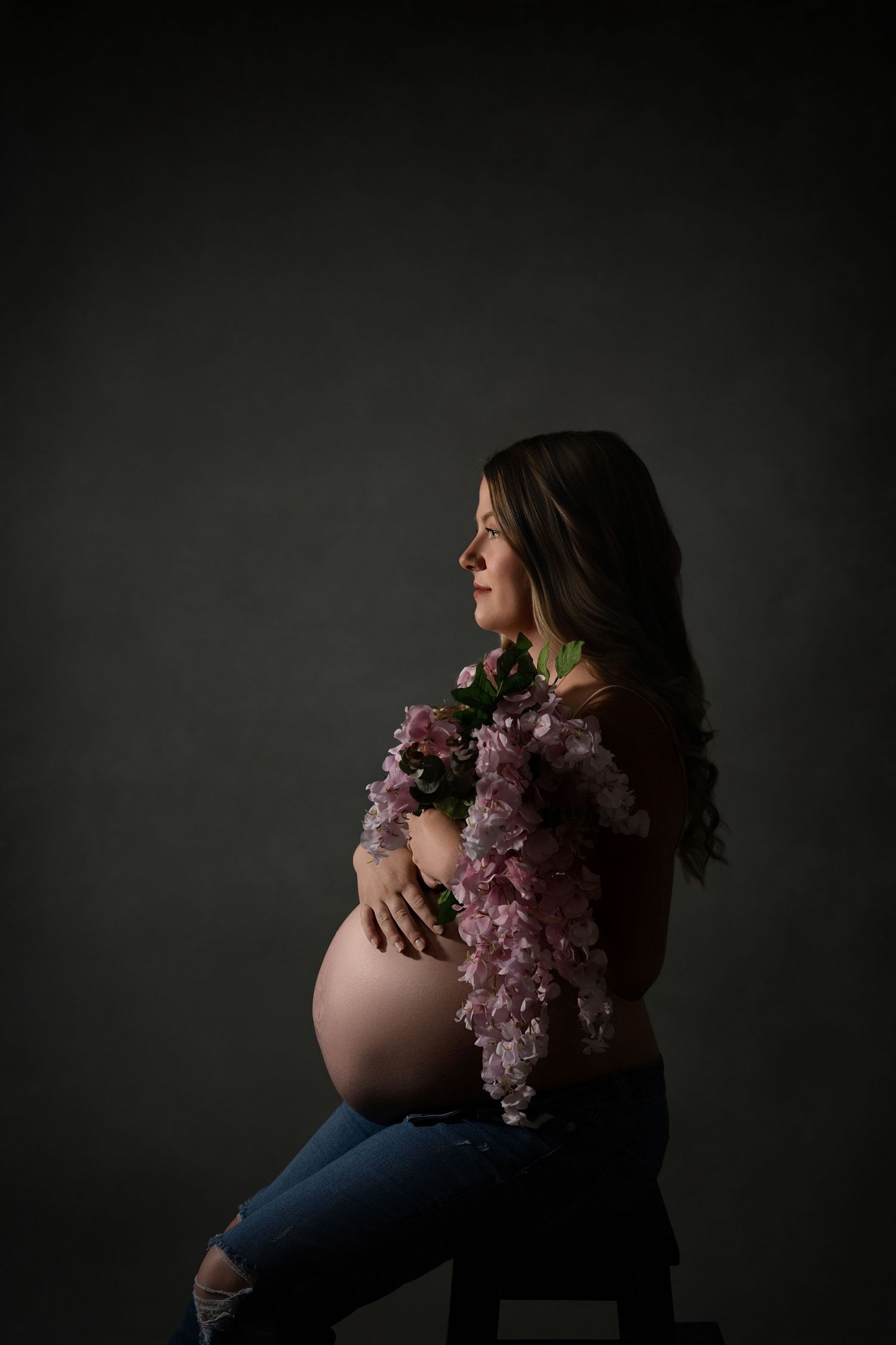 Dramatic maternity photography series showing silhouette against dark background with pink floral accents.