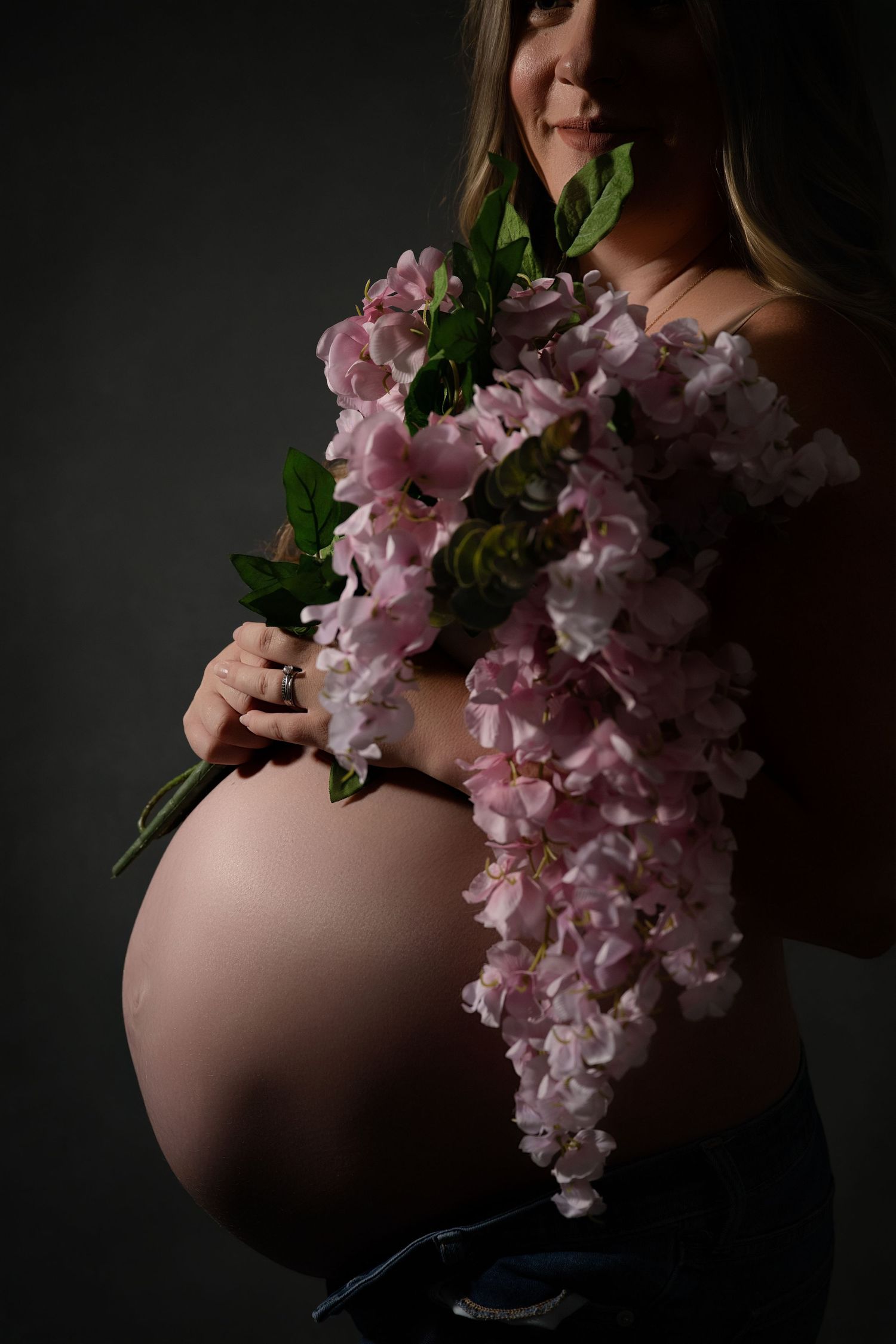 Artistic maternity photo series showing pregnant belly with delicate pink cherry blossoms against dark background.