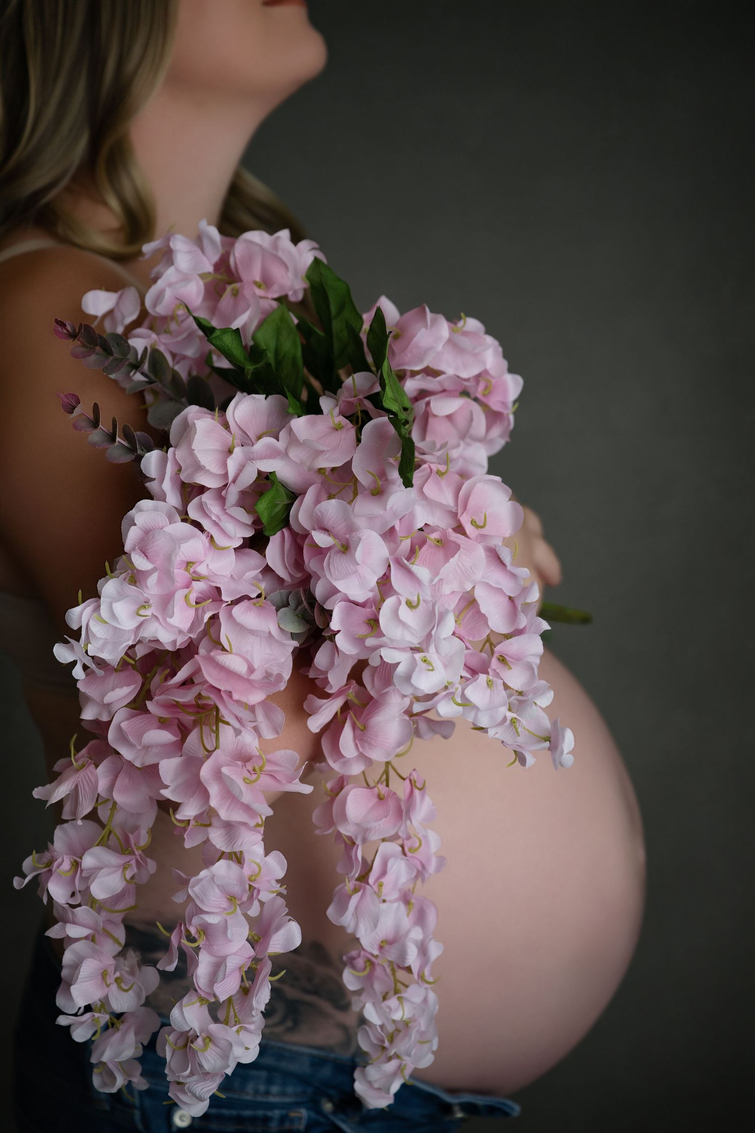 Beautiful pink hydrangea flowers cascade over a pregnant woman's belly in an artistic maternity photo series.