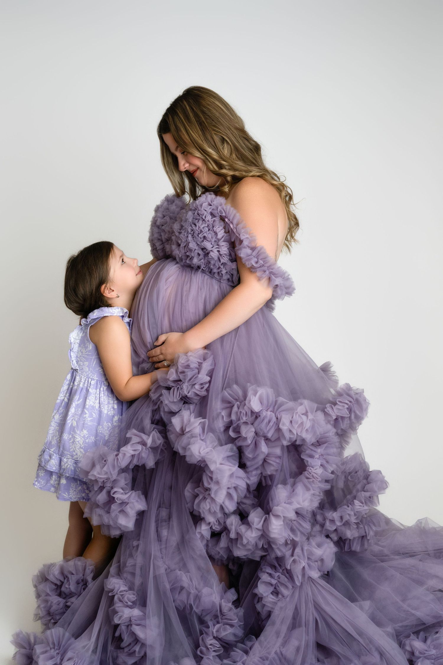 A mother and daughter share a tender embrace while wearing matching ethereal purple tulle gowns.