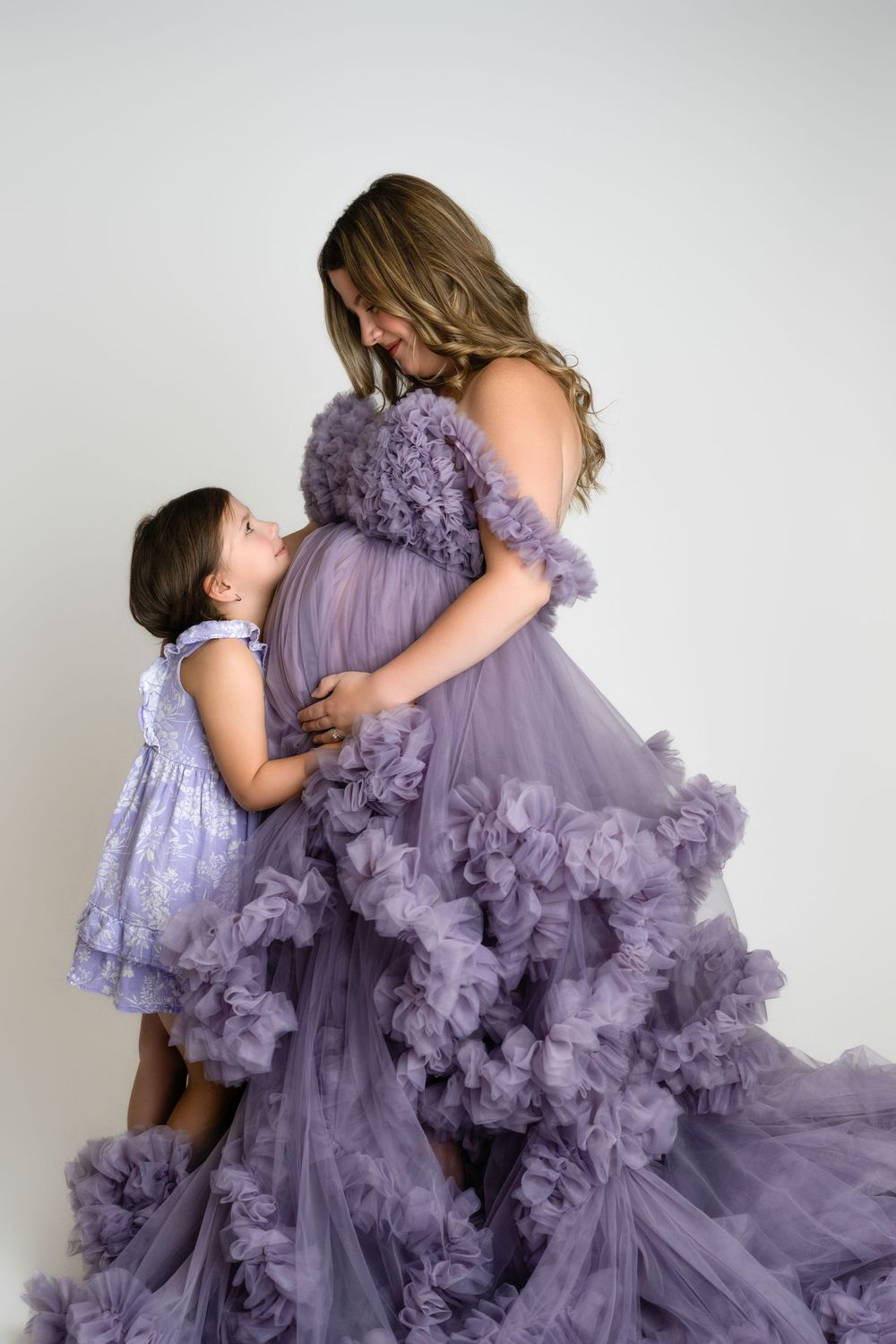 A mother and daughter share a tender embrace while wearing matching ethereal purple tulle gowns.