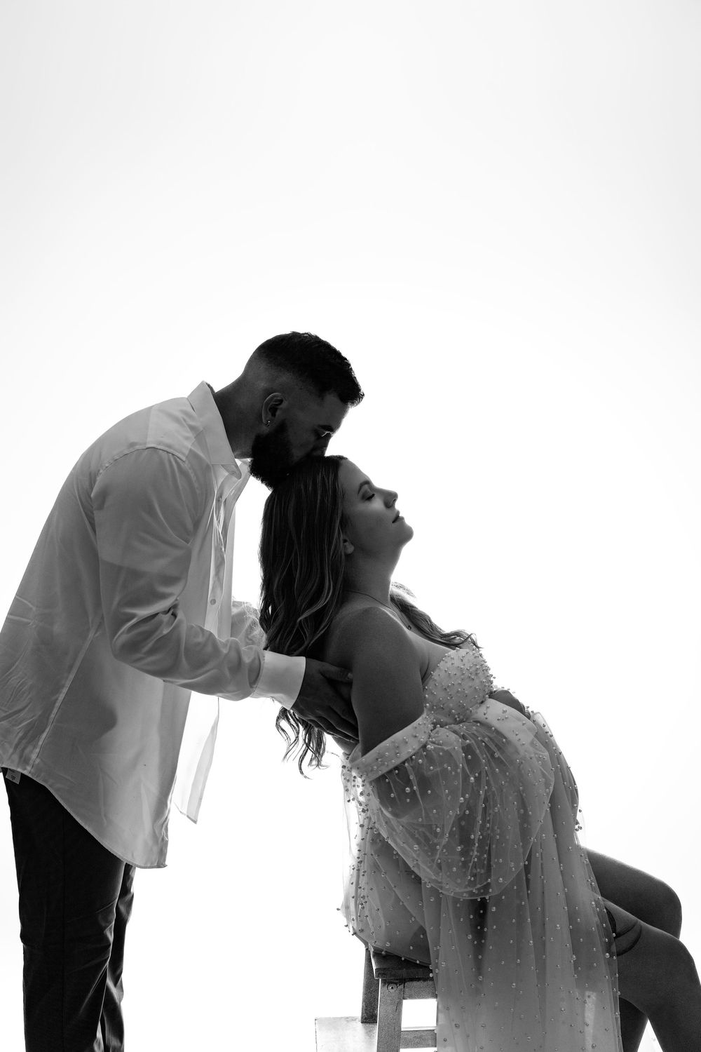 An artistic black and white silhouette photograph shows an intimate moment between a couple in wedding attire.