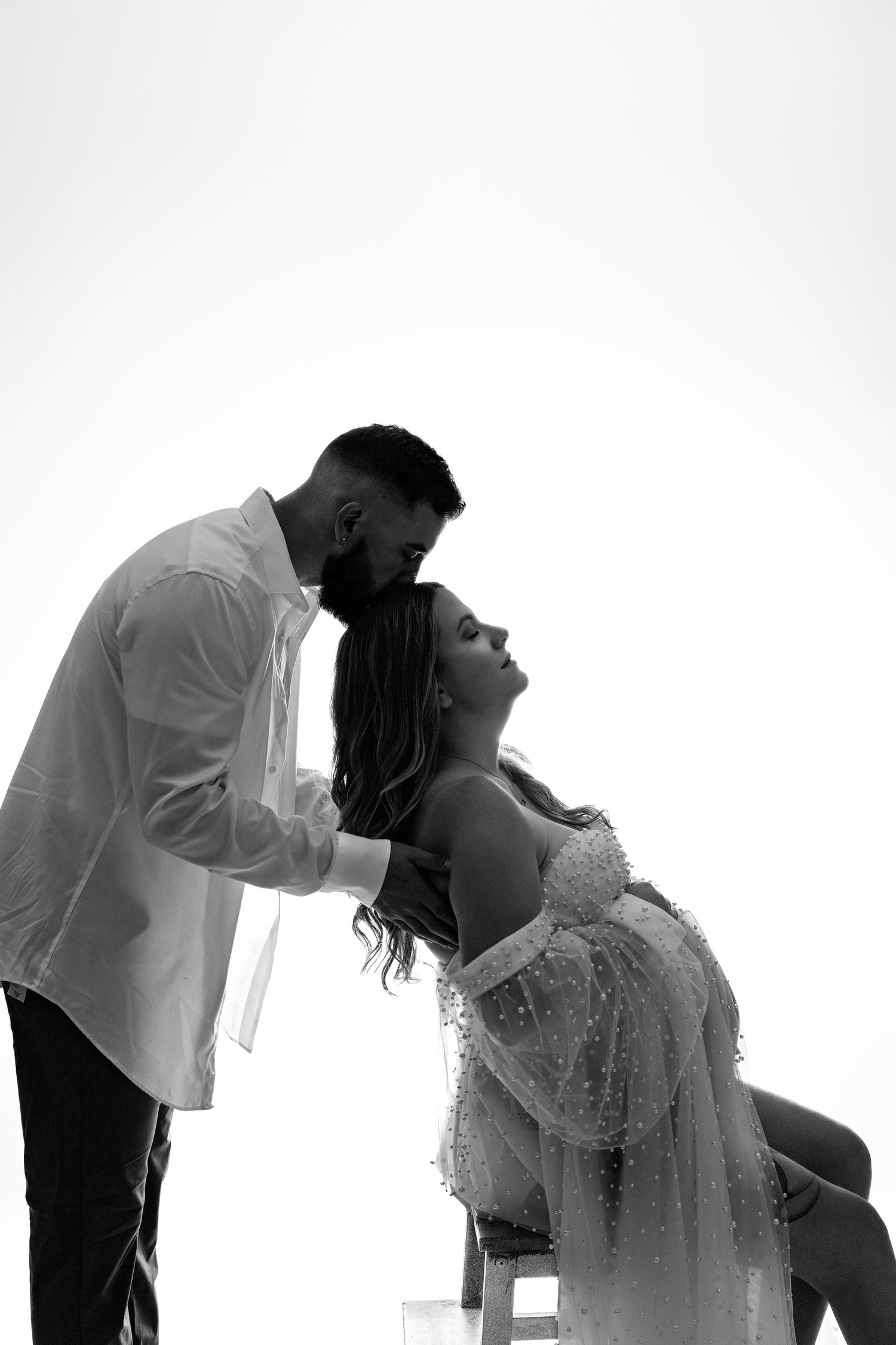 An artistic black and white silhouette photograph shows an intimate moment between a couple in wedding attire.