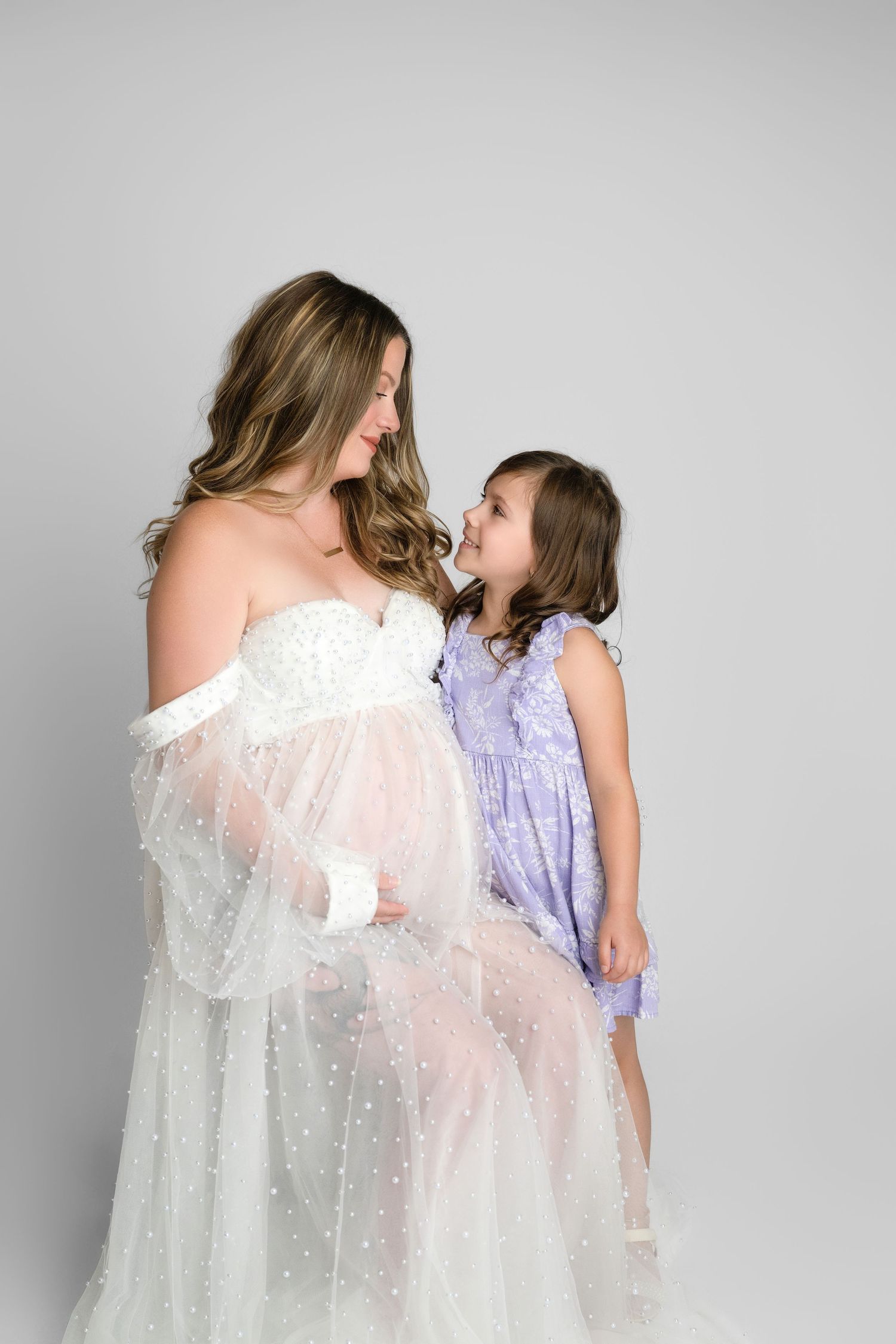 Two people in flowy dresses create an intimate moment in profile against a light gray background.