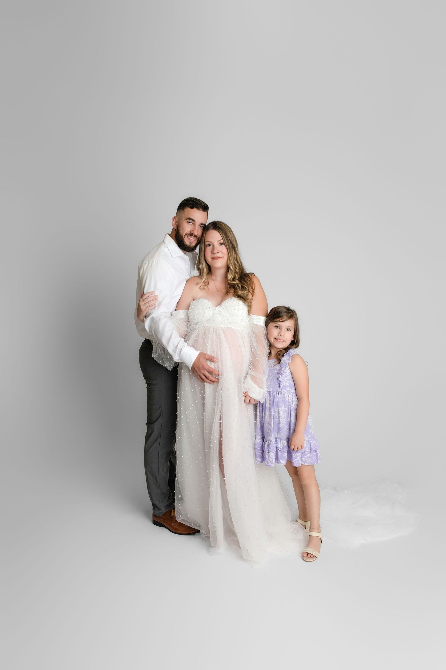A loving family in formal attire poses playfully for photos against a light gray studio backdrop.
