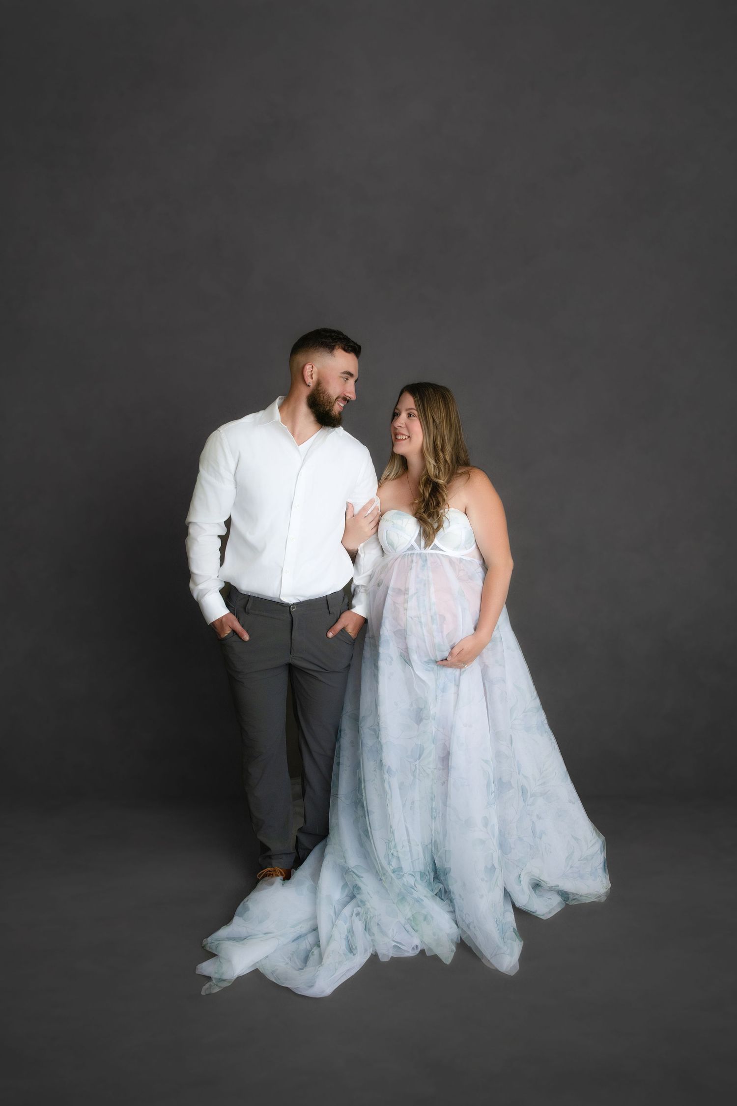 A couple in coordinated white outfits poses together against a dark backdrop in a romantic styled photoshoot sequence.