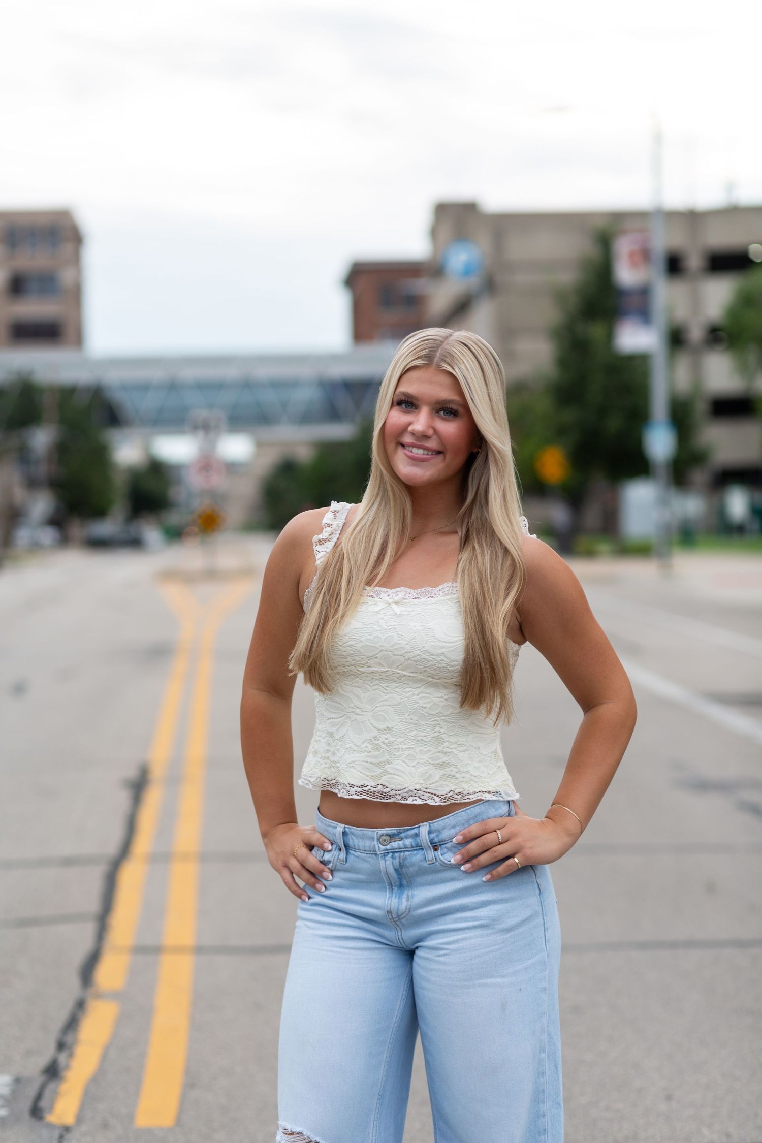 An urban street photoshoot featuring light blue jeans and a white crop top against a backdrop of road markings.