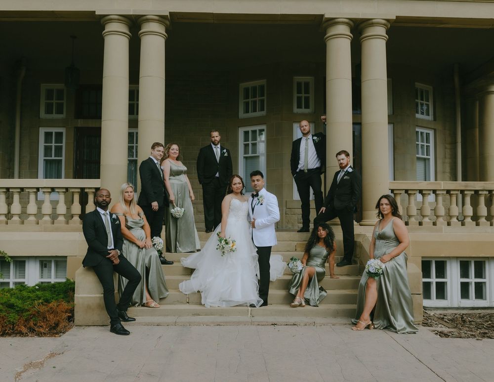 Wedding party members stand near elegant stone pillars and columns at outdoor venue with classic architecture.
