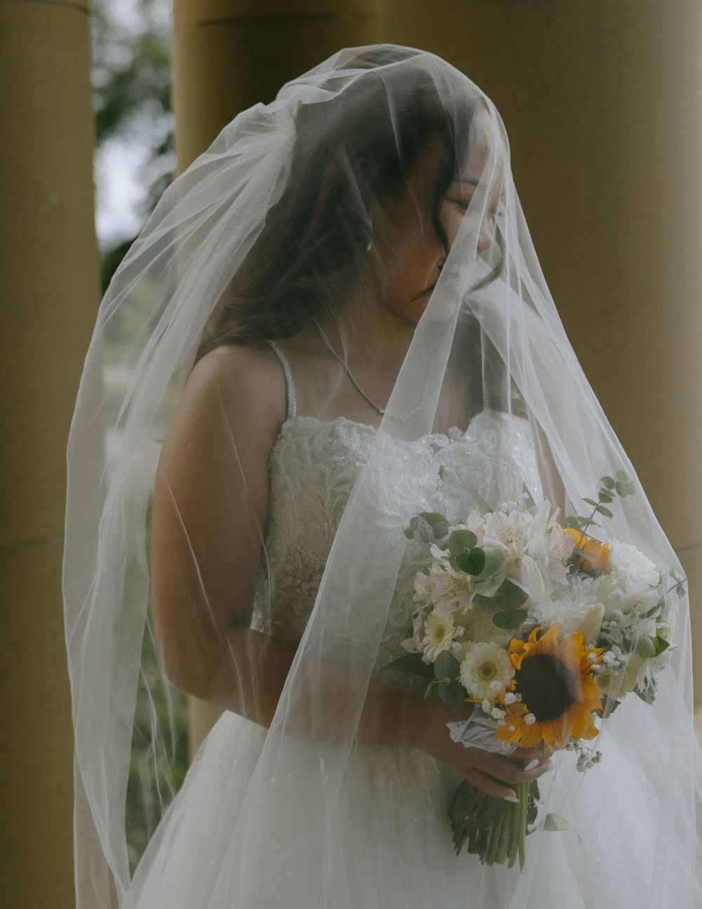 A bride in a white wedding dress and veil holds a colorful bouquet with yellow and white flowers.