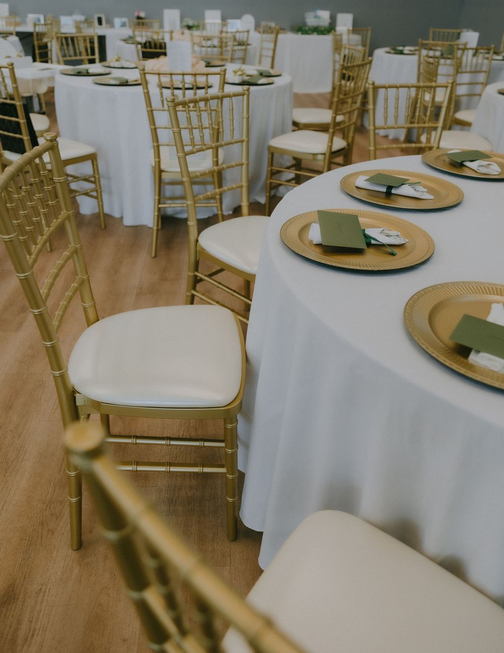Gold chiavari chairs and round tables with white linens and gold charger plates set up for an elegant wedding reception.