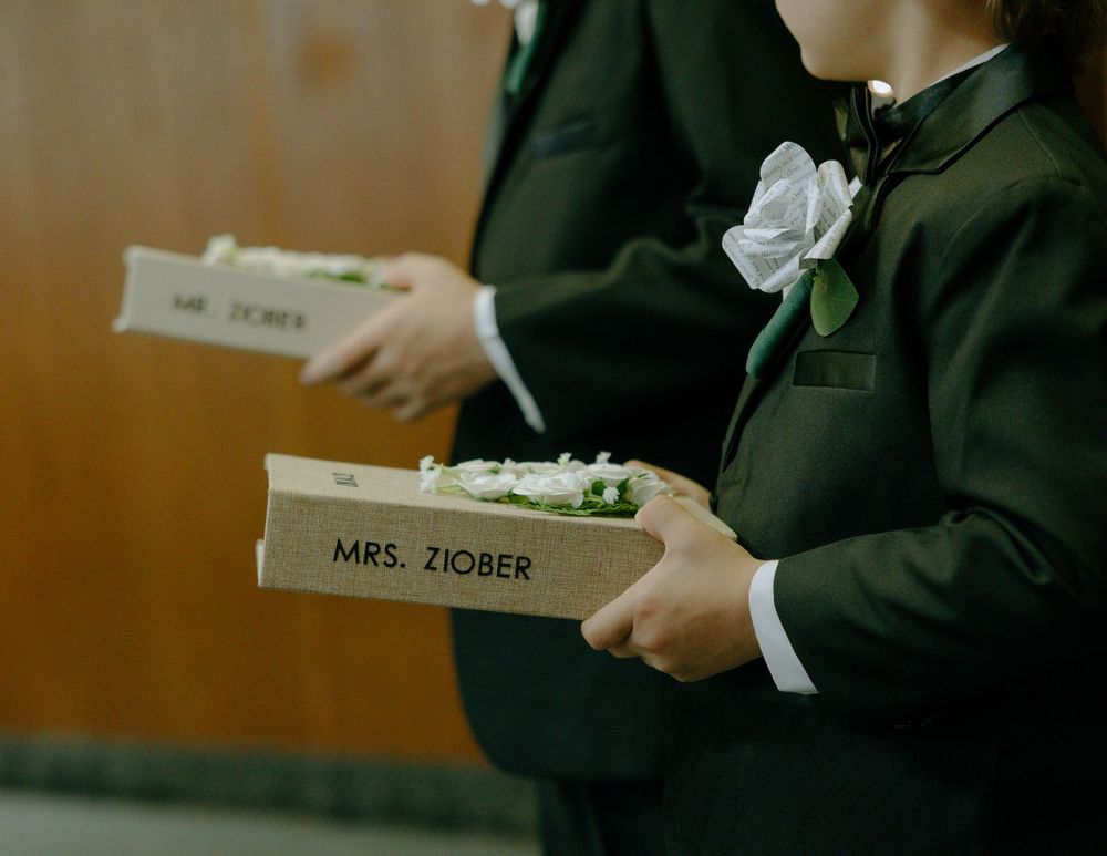 Two groomsmen in dark suits holding name cards decorated with white floral boutonnieres.