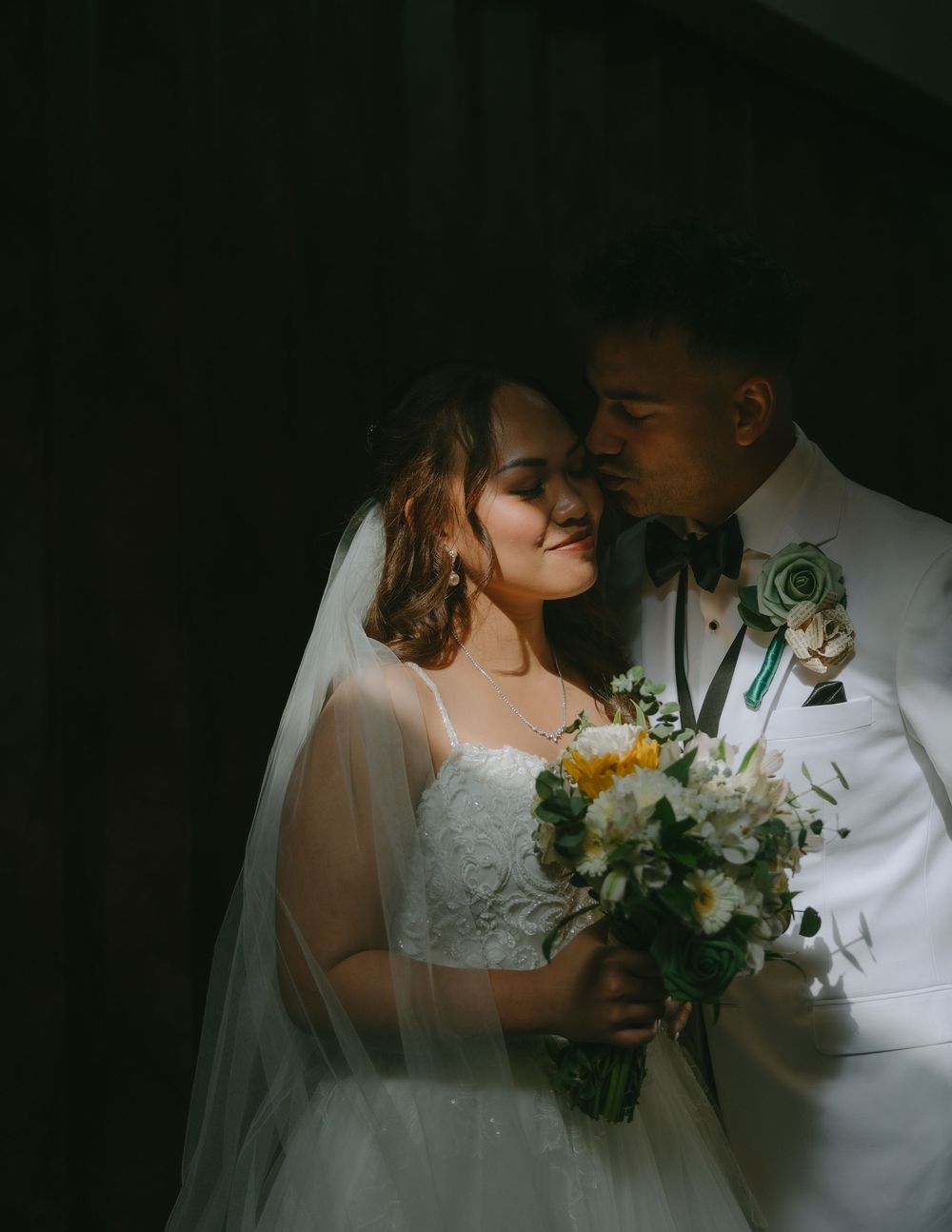 A romantic silhouette of newlyweds embracing in dramatic lighting with a floral bouquet.