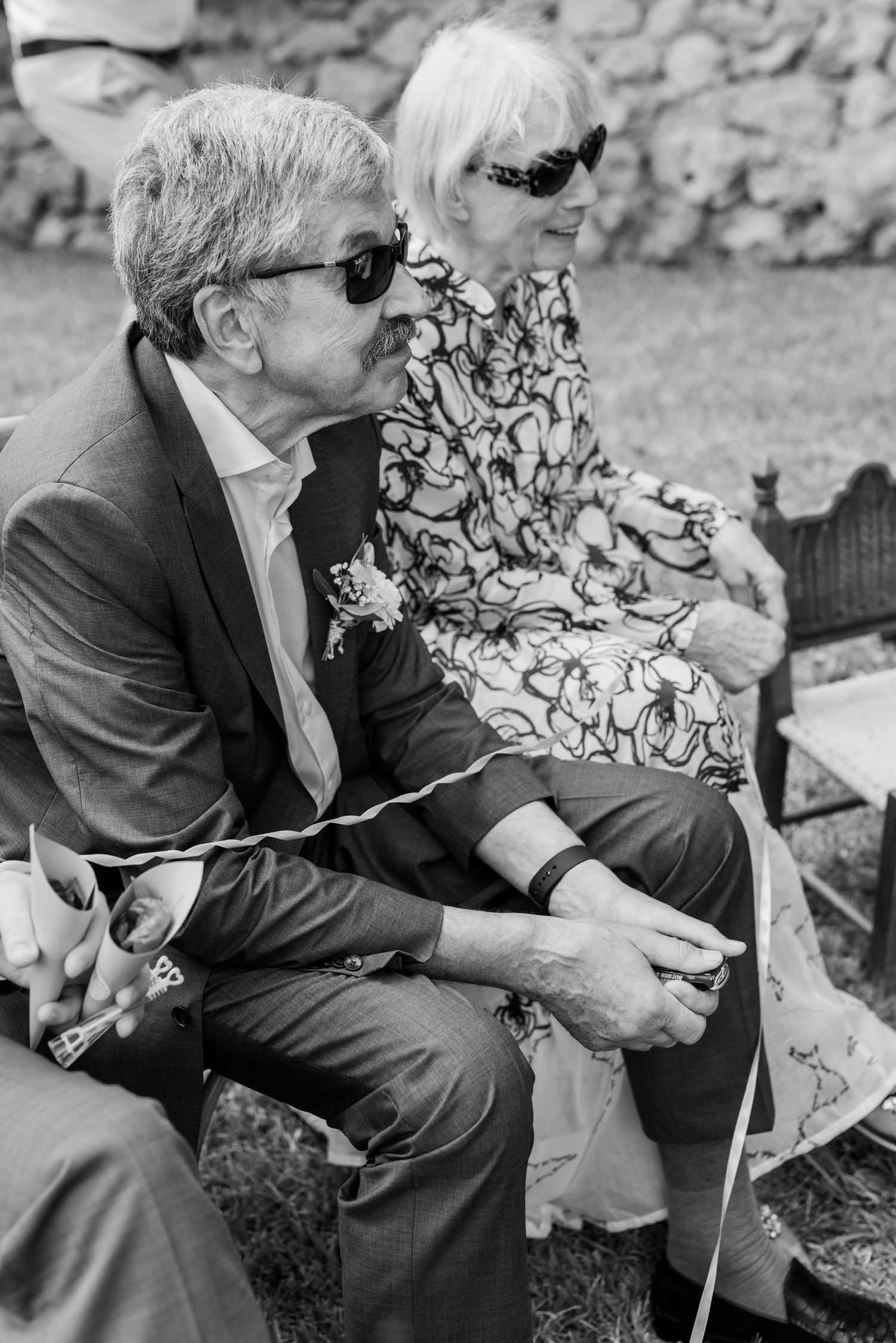 Das Schwarz-Weiß-Foto zeigt die Eltern des Bräutigams in schicker Kleidung, die sitzen und das Brautpaar außerhalb des Bildausschnitts sehen