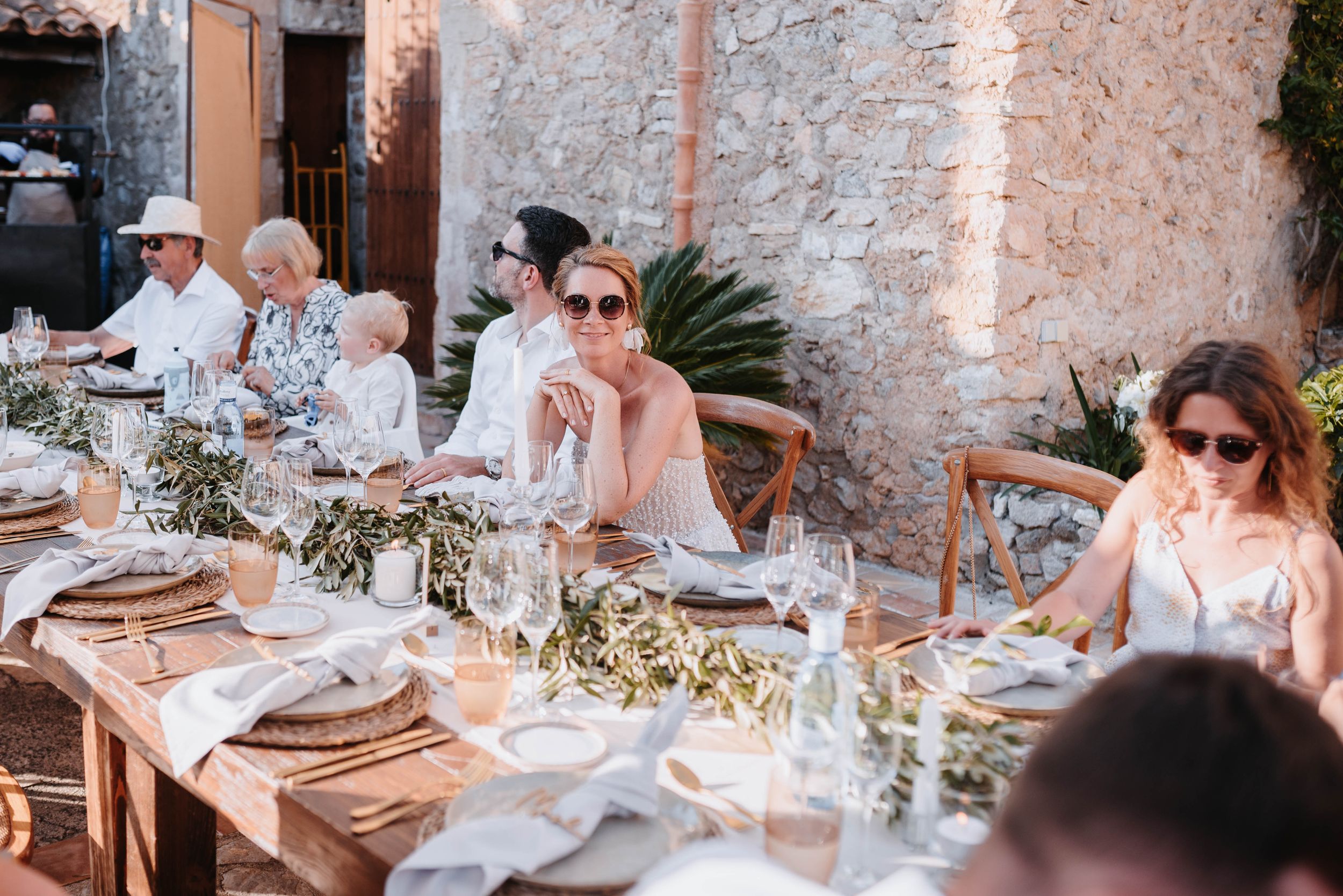 People enjoying an elegant outdoor dinner party at a rustic stone venue with decorated table settings and string lights.