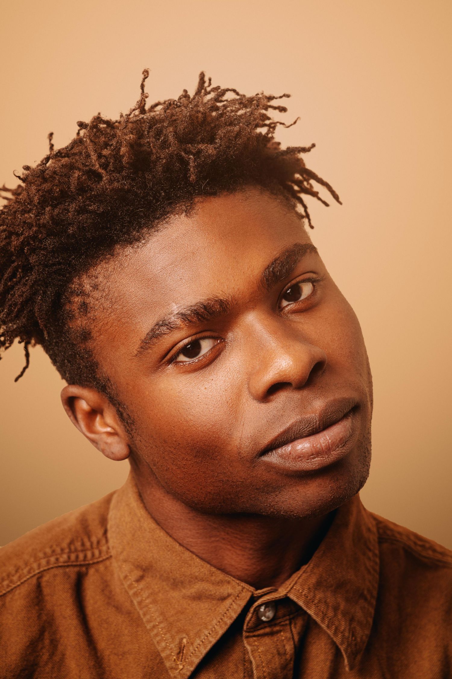 Portrait of person in brown shirt against warm orange background.