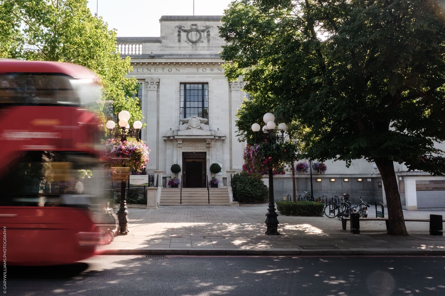 A classic London street scene with a blurred red double-decker bus passing by a white neoclassical building entrance.