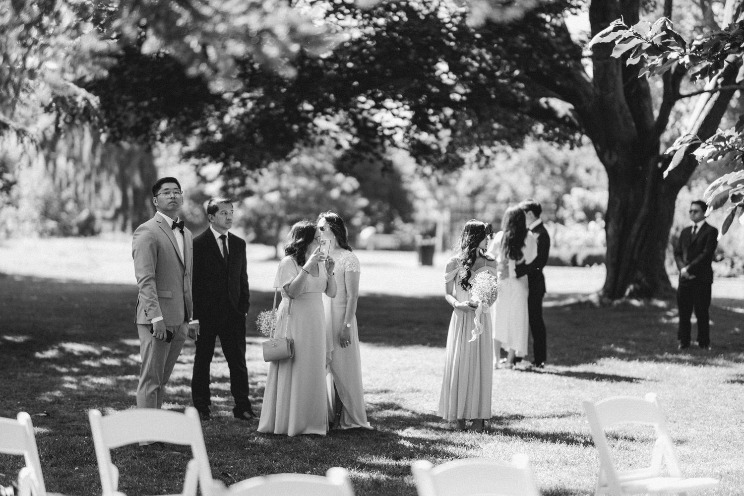 A black and white photo of a small group standing together during an outdoor wedding ceremony in a park.