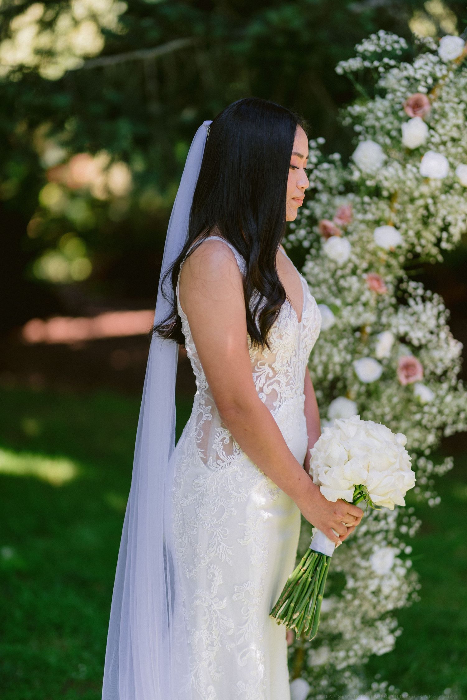 An elegant lace wedding gown with flowing veil against a garden backdrop.