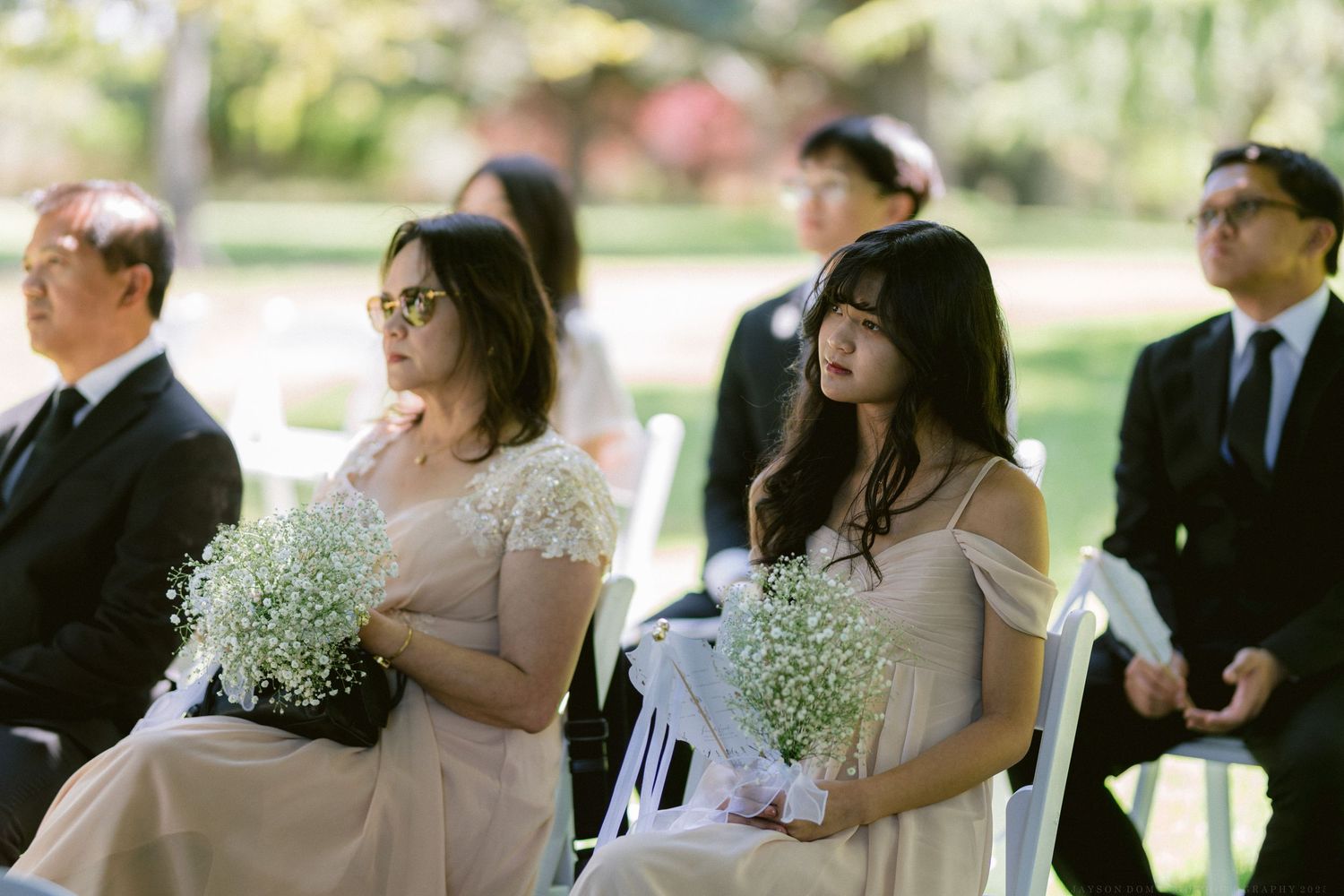 A beautiful outdoor wedding ceremony unfolds with guests and attendees gathered in a serene garden setting.