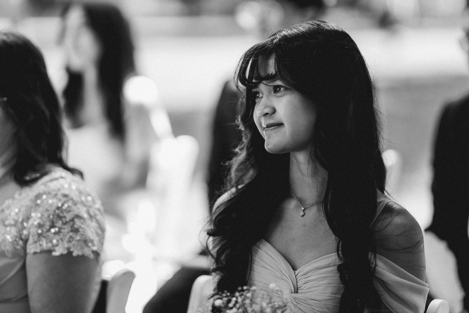 Black and white photo of a woman with long dark hair in a strapless dress looking to the side with a dreamy expression.