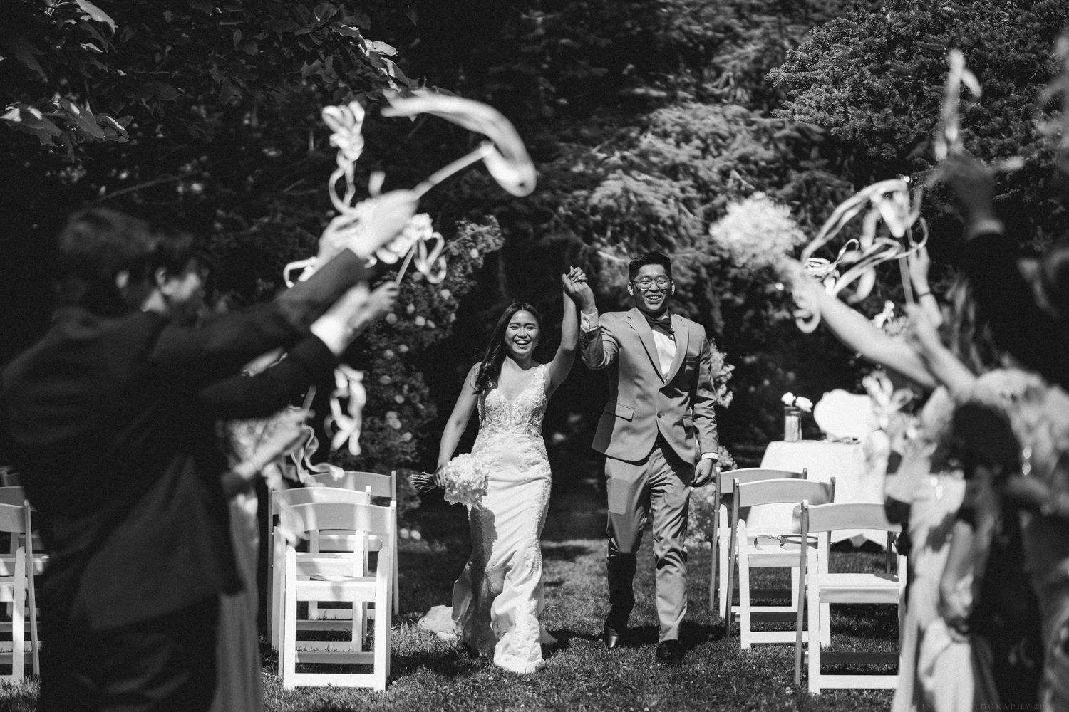 Wedding party and guests joyfully tossing rose petals in the air during an outdoor celebration.