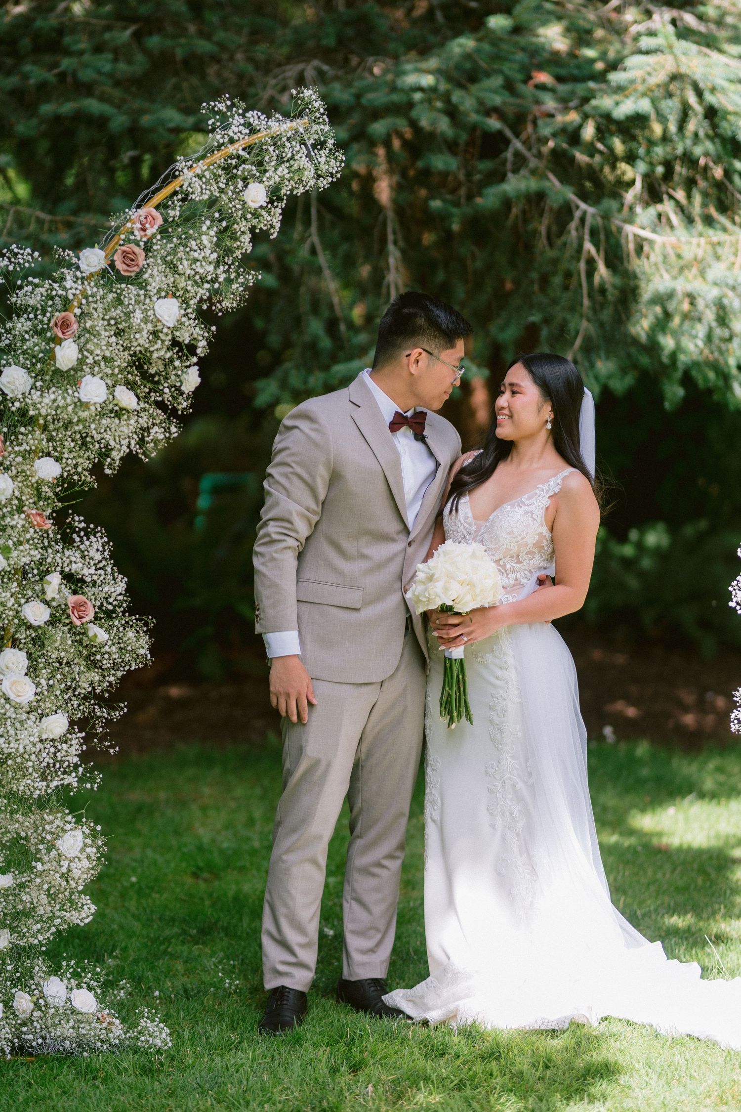 Newlyweds share an intimate moment under a floral arch at their outdoor garden wedding.