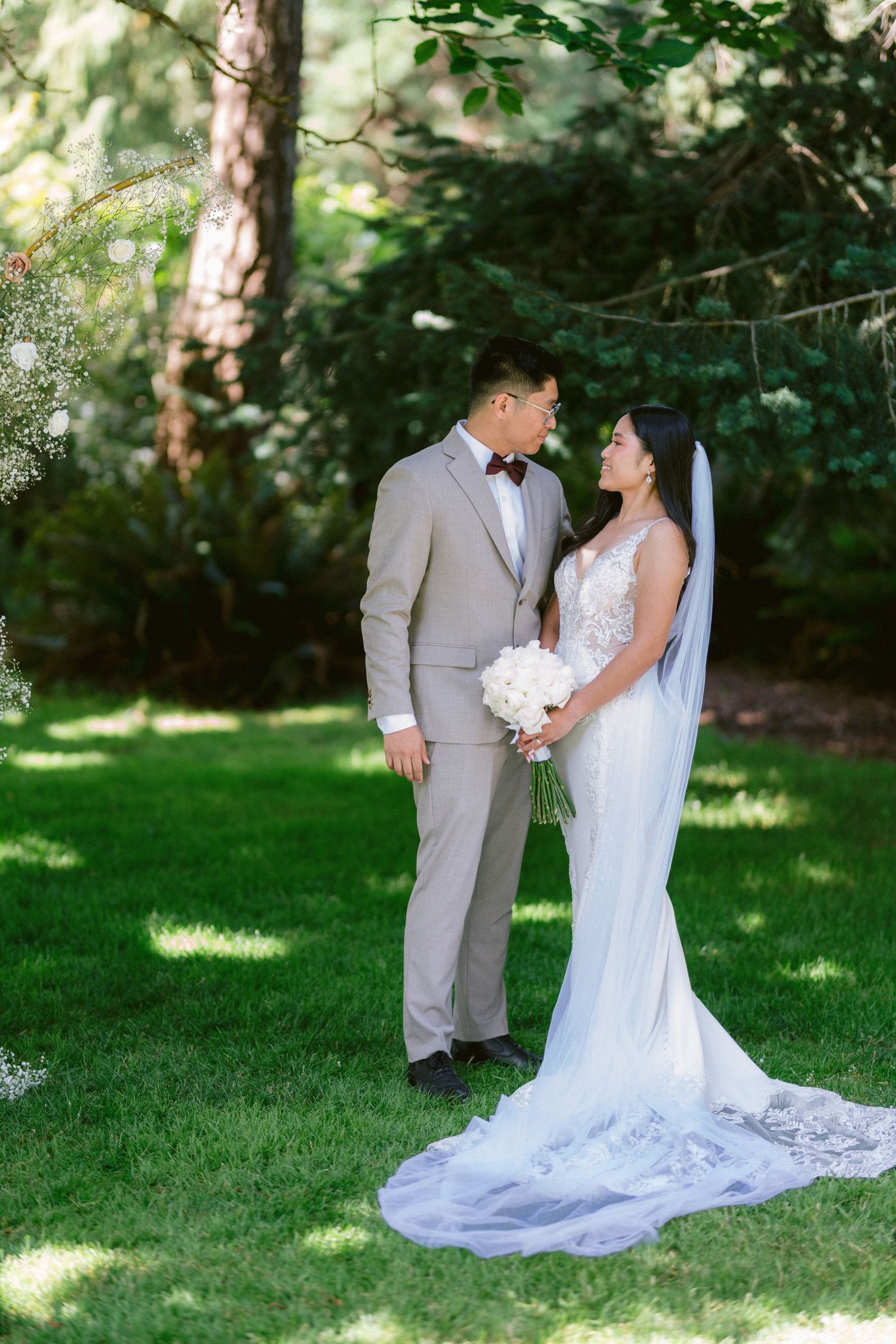 Elegant couple poses for wedding portraits in a sunlit garden setting.