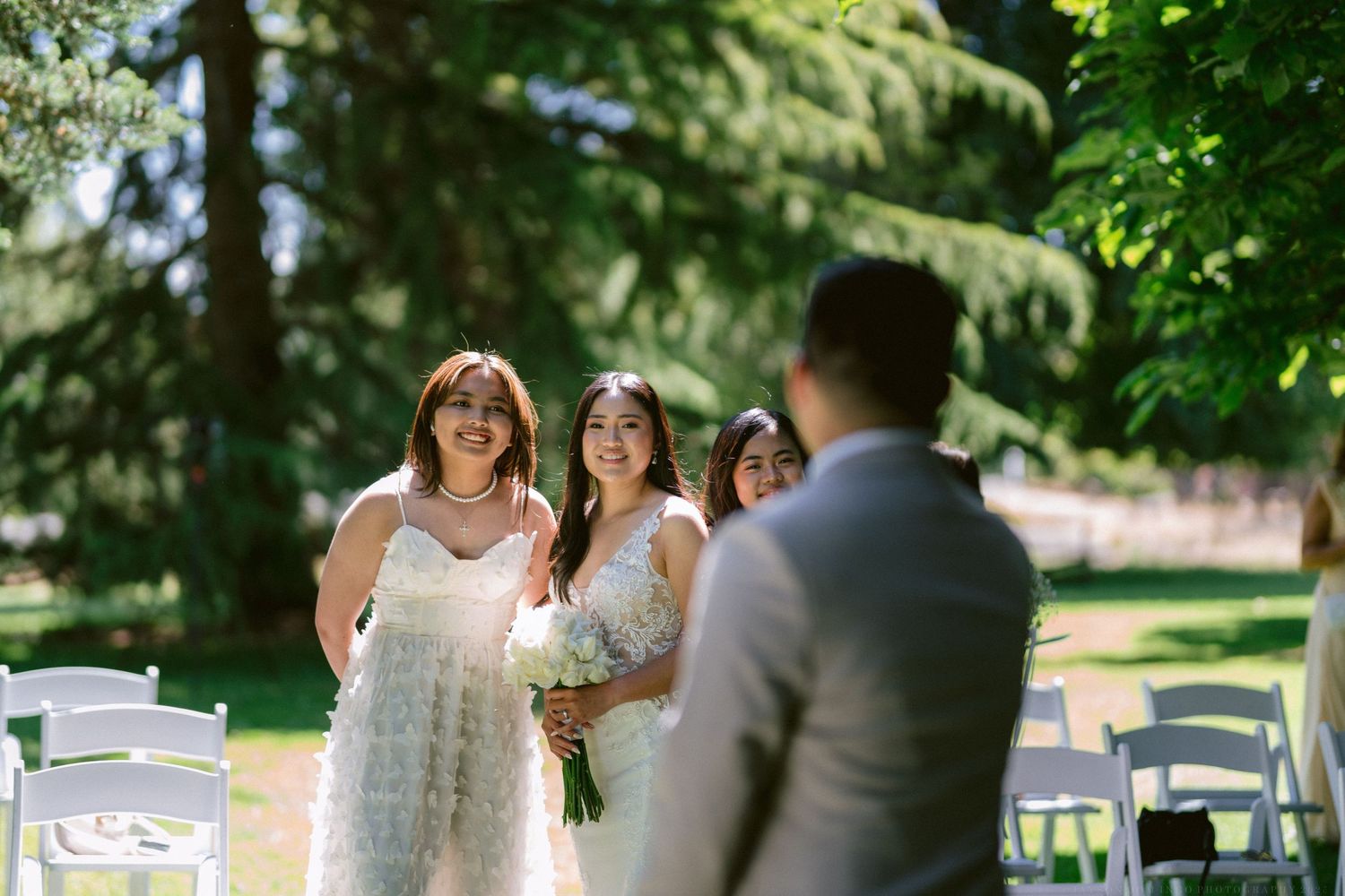 An outdoor wedding ceremony in a sunlit garden with white folding chairs arranged on the lawn.