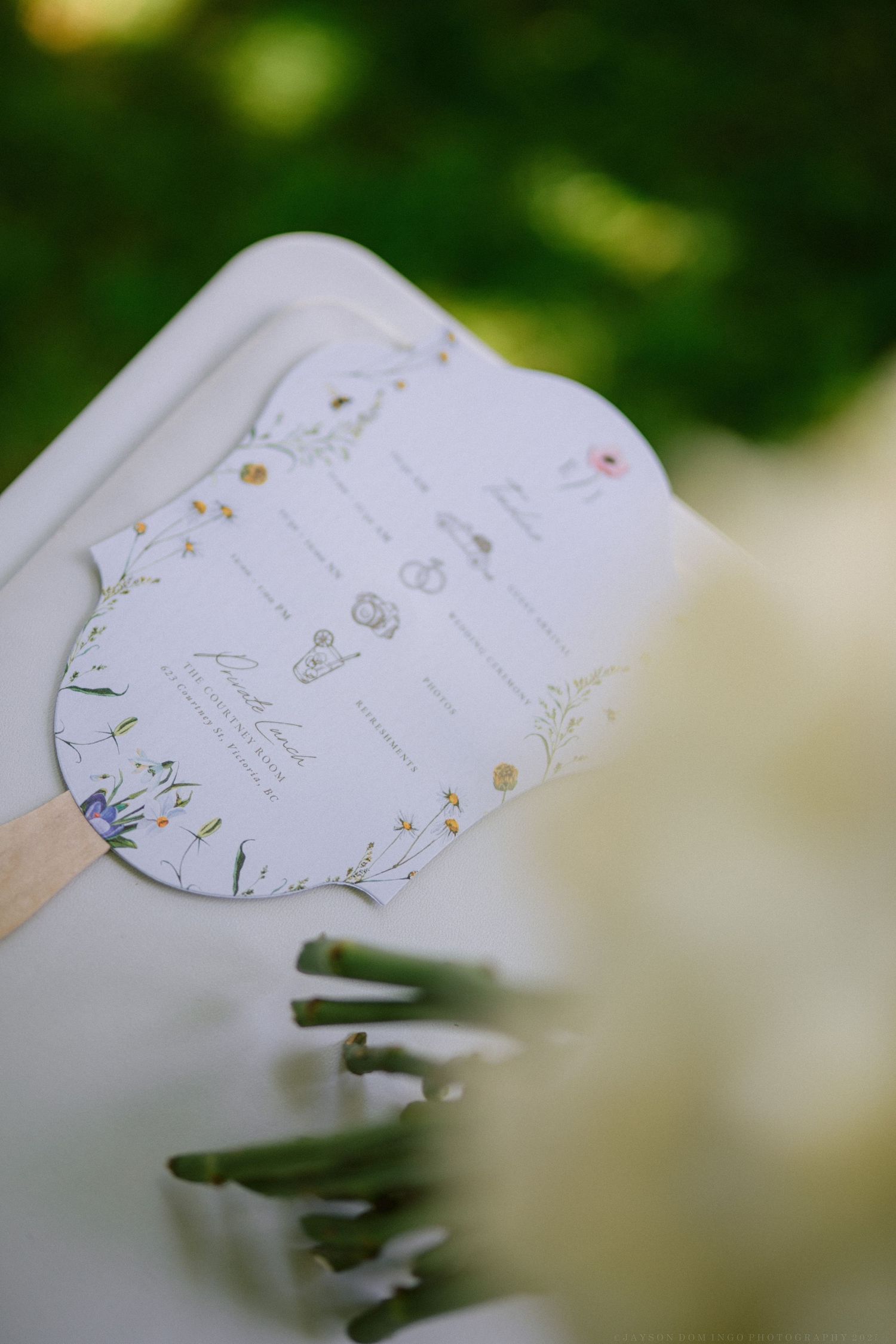 A wedding program or ceremony details card with delicate floral decorations held against a blurred green background.