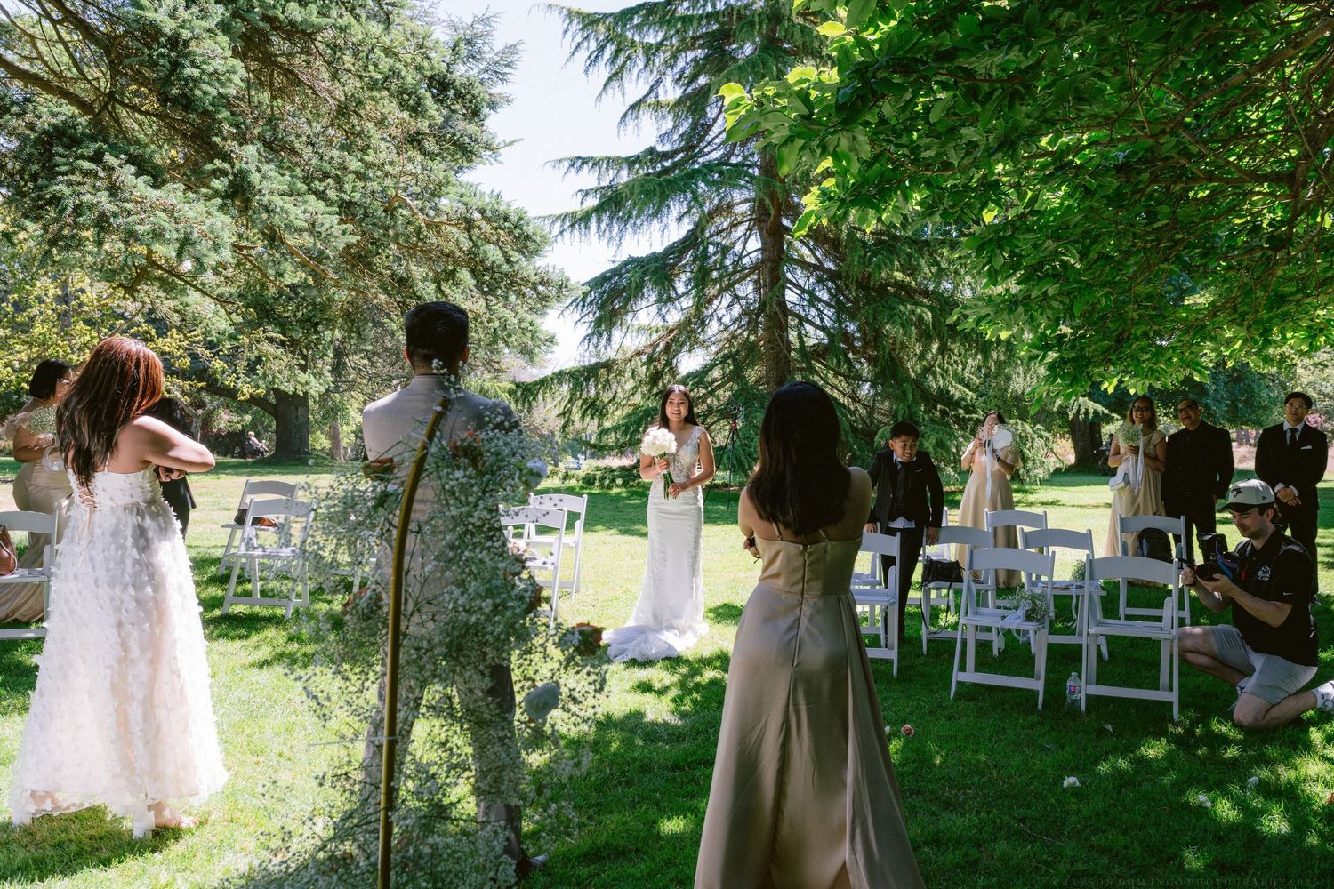 An outdoor wedding ceremony setup in a garden with white chairs and guests mingling.