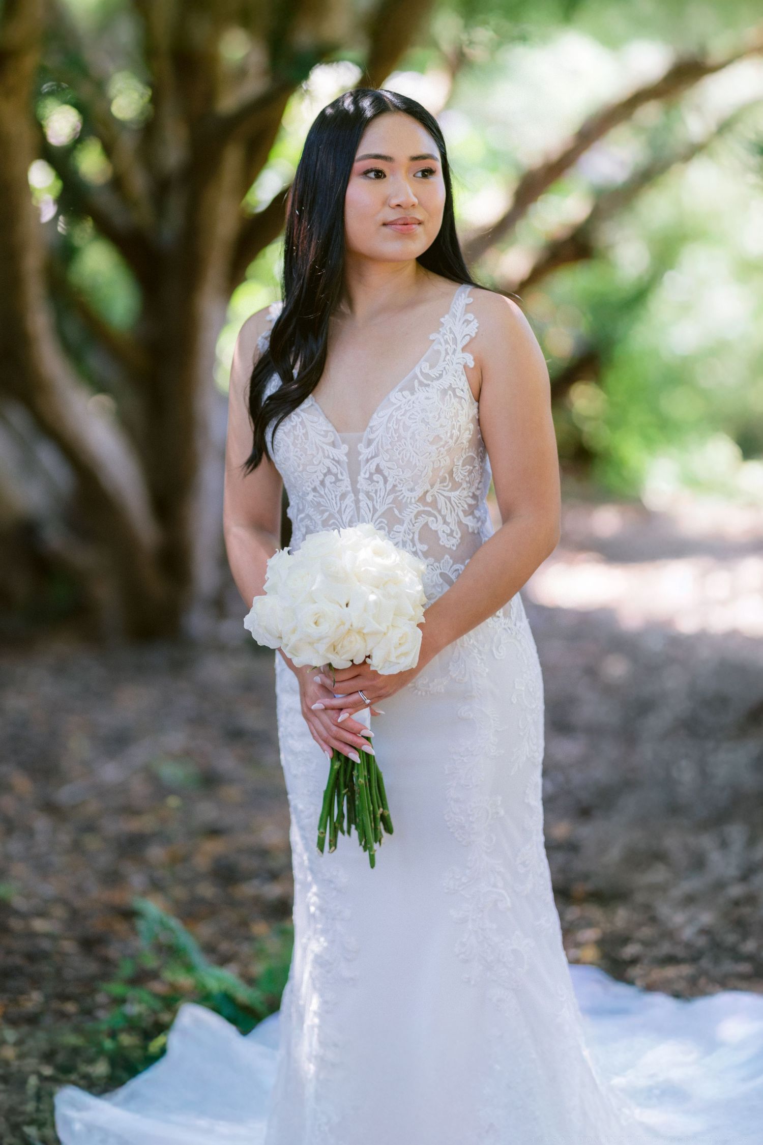 Elegant wedding dress with lace details and white bouquet in outdoor garden setting.