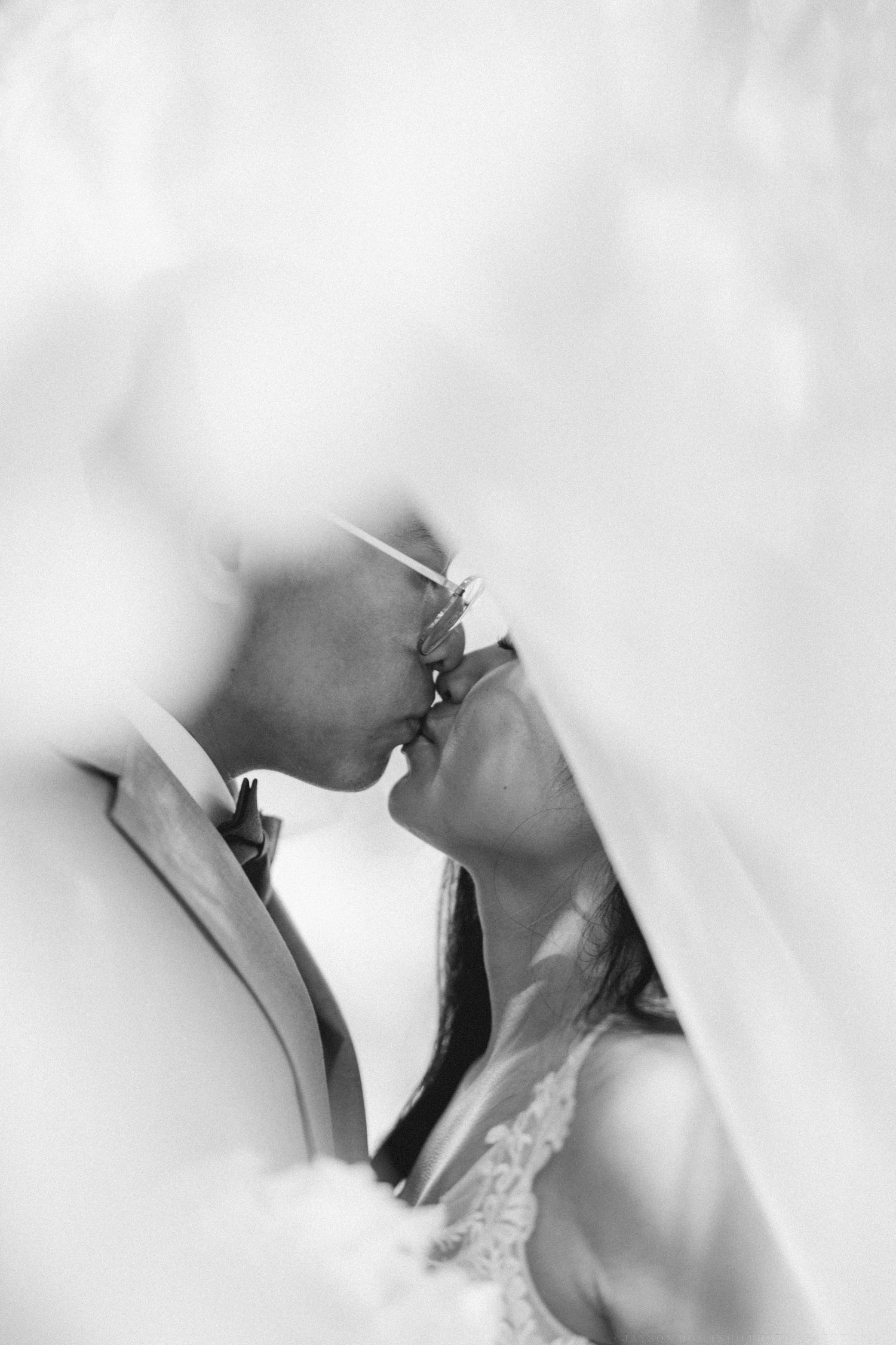 A romantic black and white wedding portrait showing a tender kiss through soft focus.