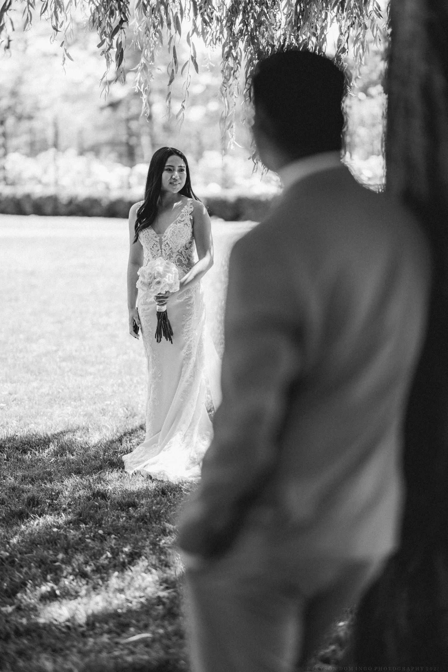 Black and white wedding portrait of bride and groom under willow trees.