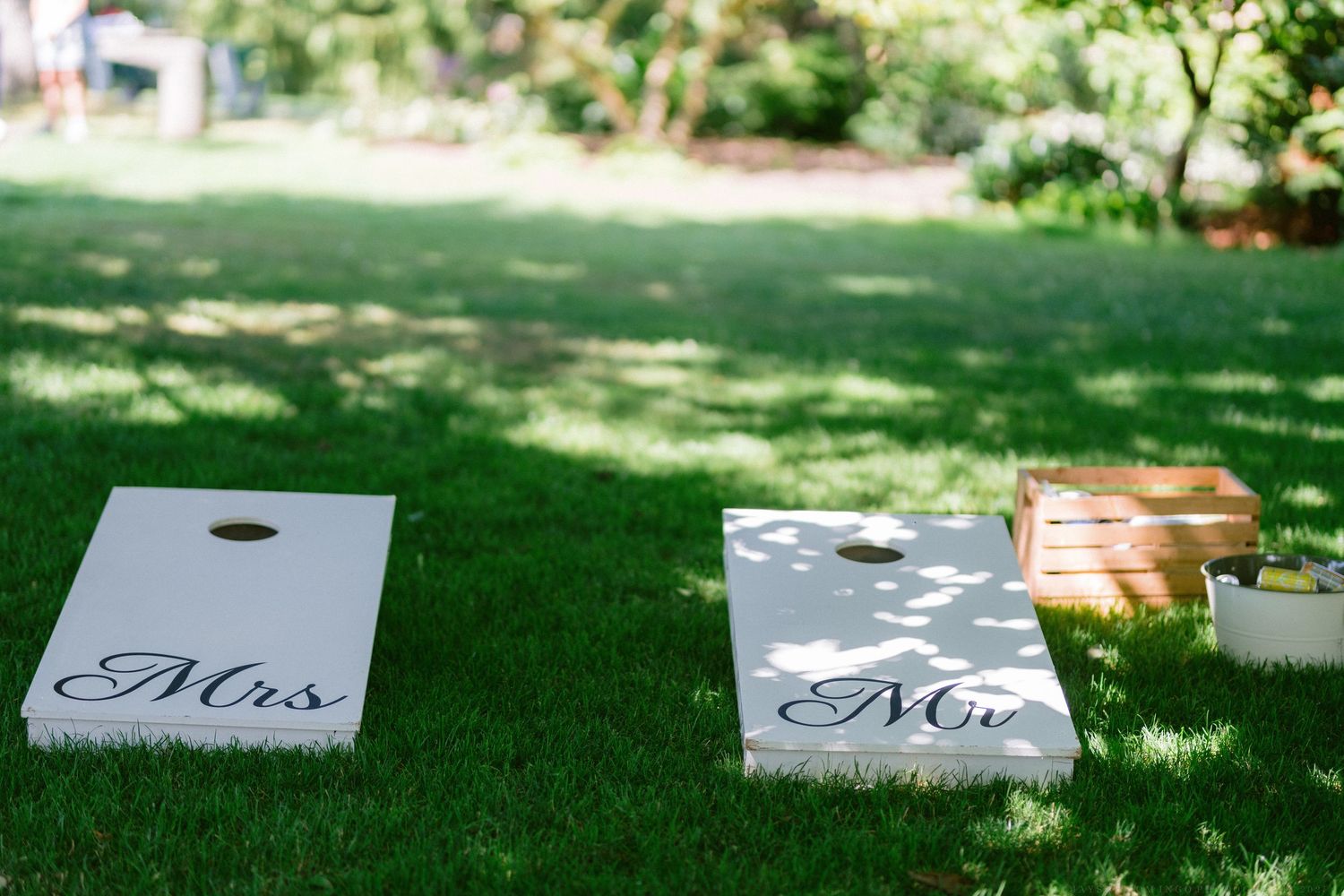 White cornhole boards set up for a wedding game with decorative Mrs. sign visible on grass lawn.