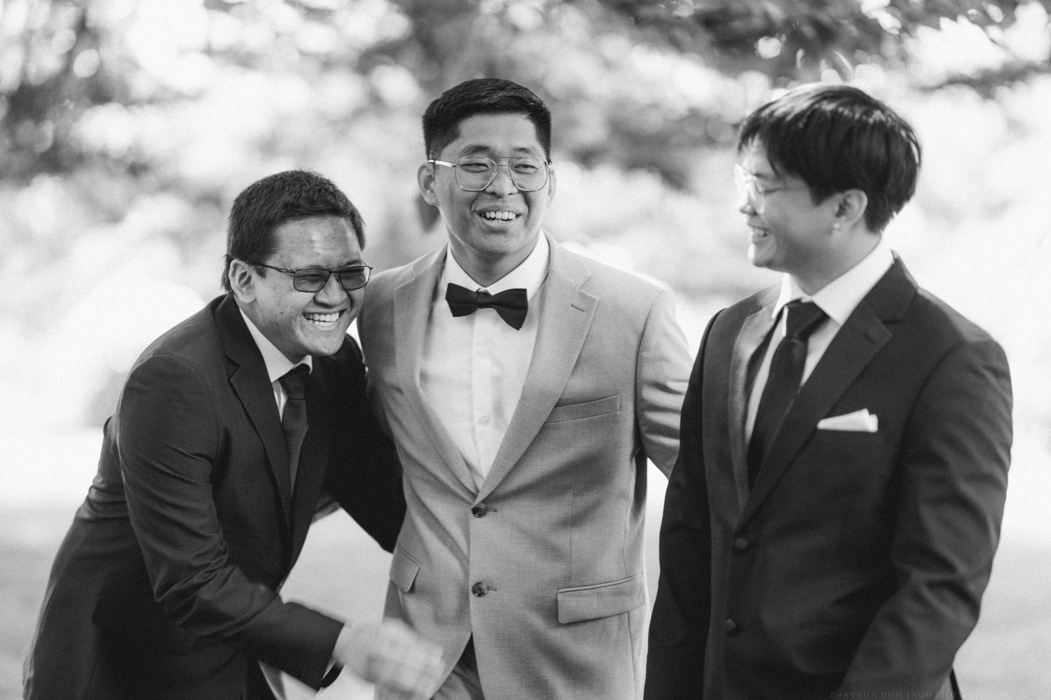 People sharing laughter and joyful moments at an outdoor wedding in black and white.