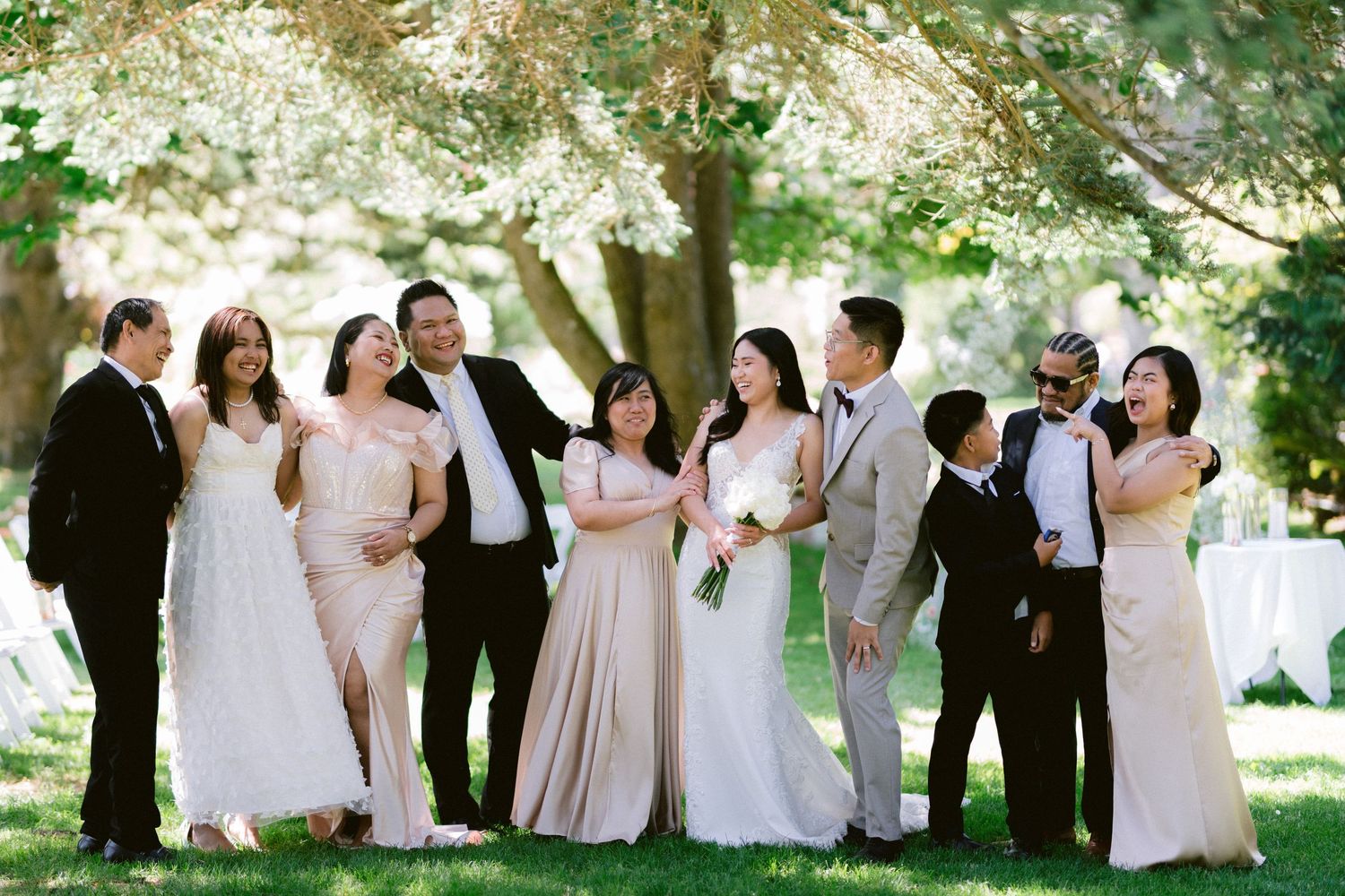 Wedding party poses together under trees in formal attire with pink bridesmaid dresses.