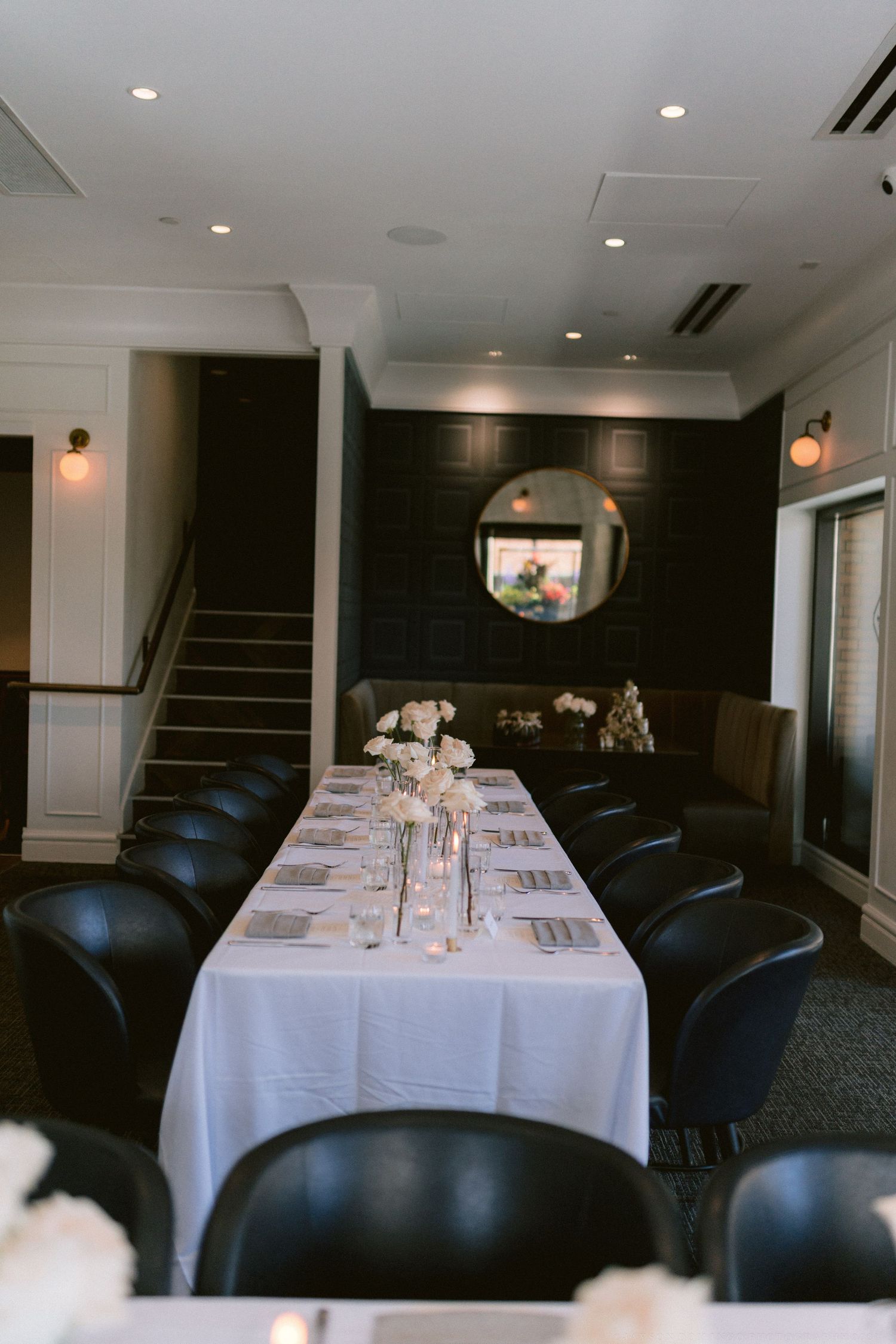 Formal dining room with long white-clothed table and black chairs set for an intimate wedding dinner.