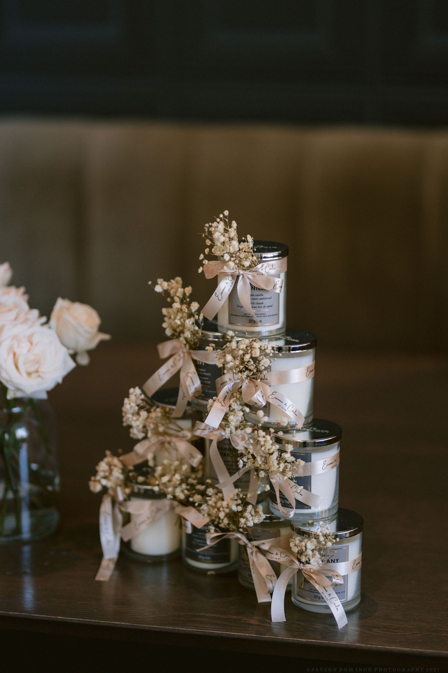 Decorative wedding favors arranged in stacked jars adorned with baby's breath and ribbons.
