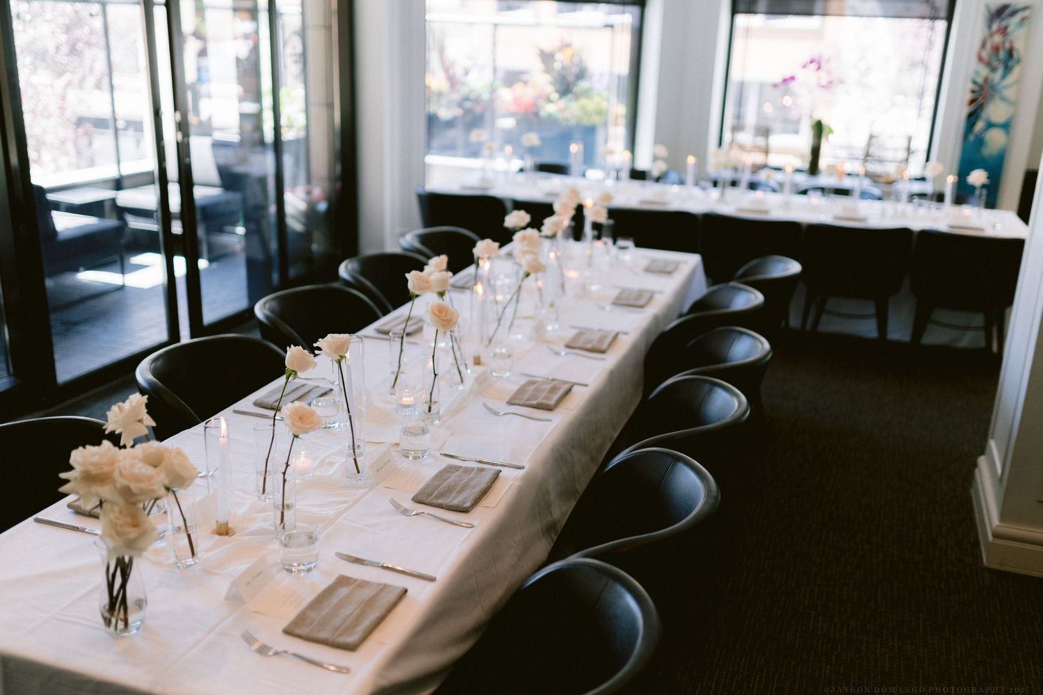 Minimalist wedding reception table set with white linens and delicate floral centerpieces.
