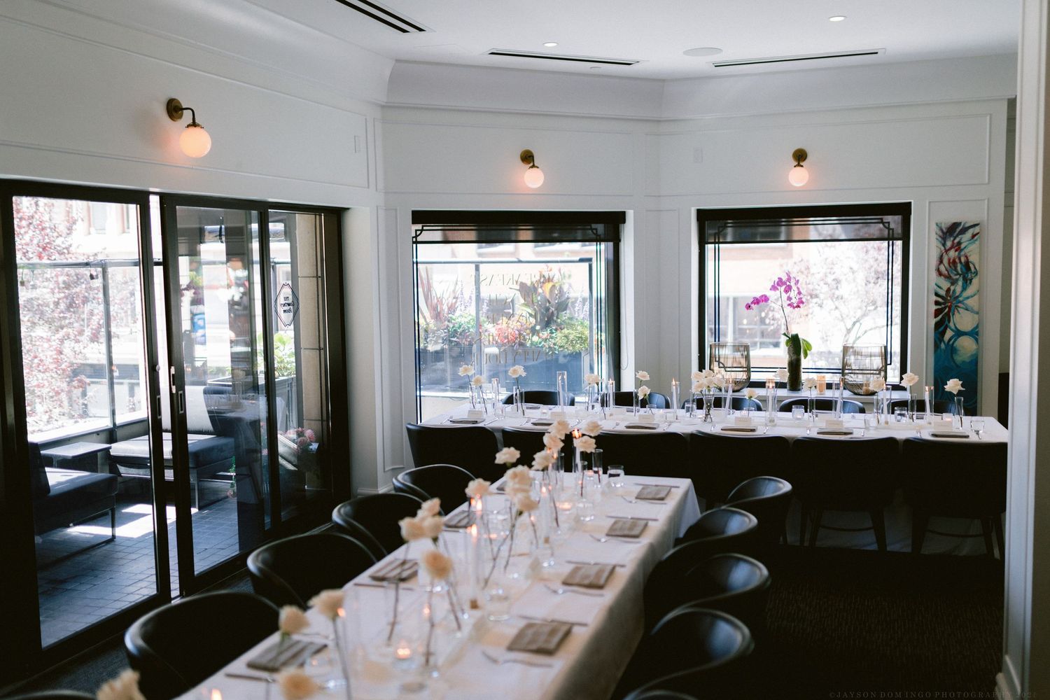 An elegant dining room with large windows set for a formal dinner reception with white tablecloths and warm lighting.