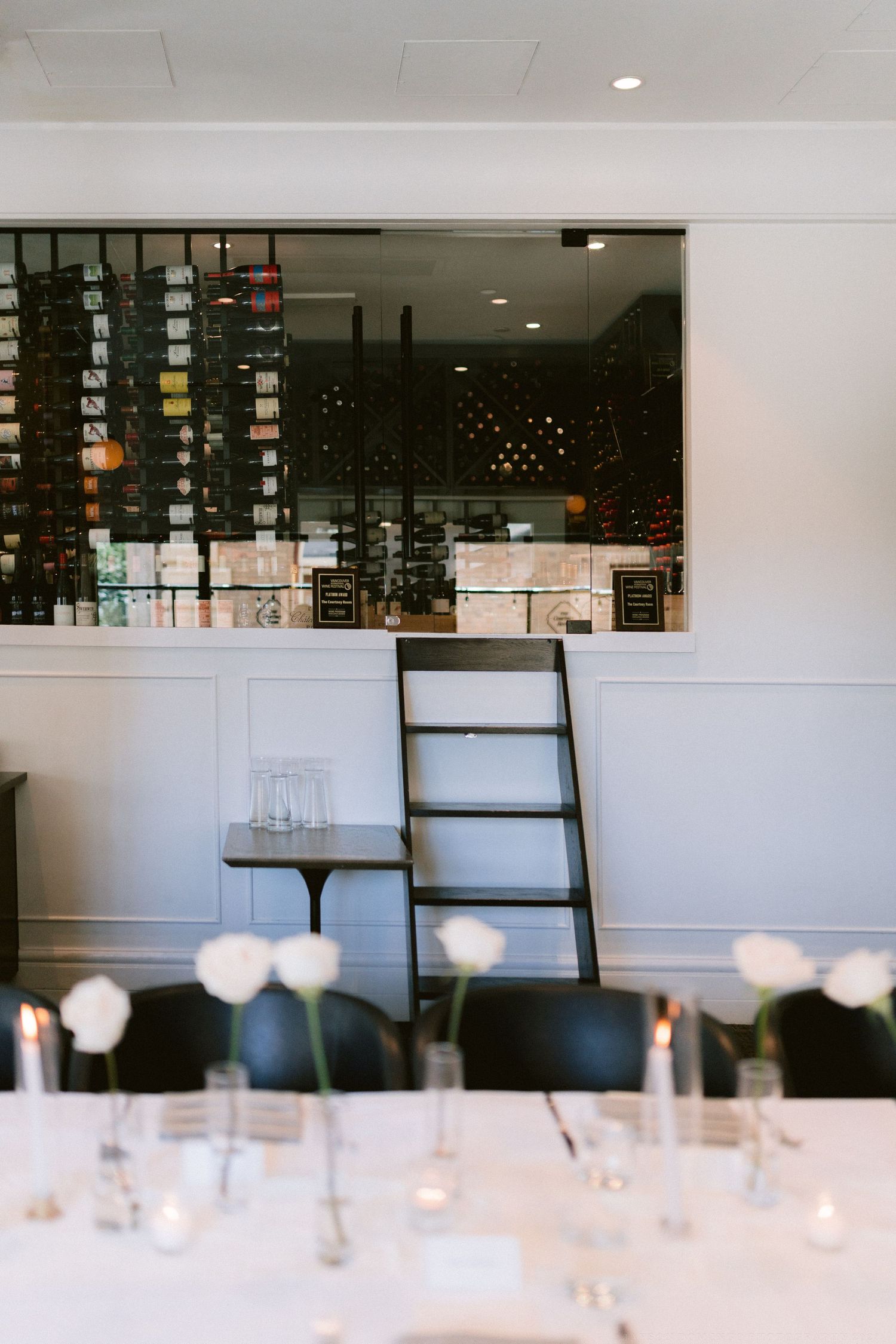 Elegant restaurant interior with wine storage display and table settings featuring glowing candles and white floral centerpieces.