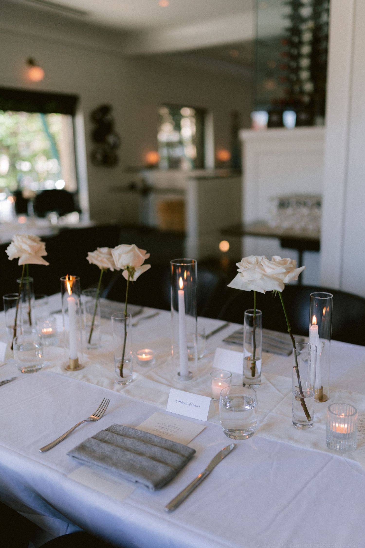 Elegant table setting with single stem roses in glass vases and glowing candlelight.