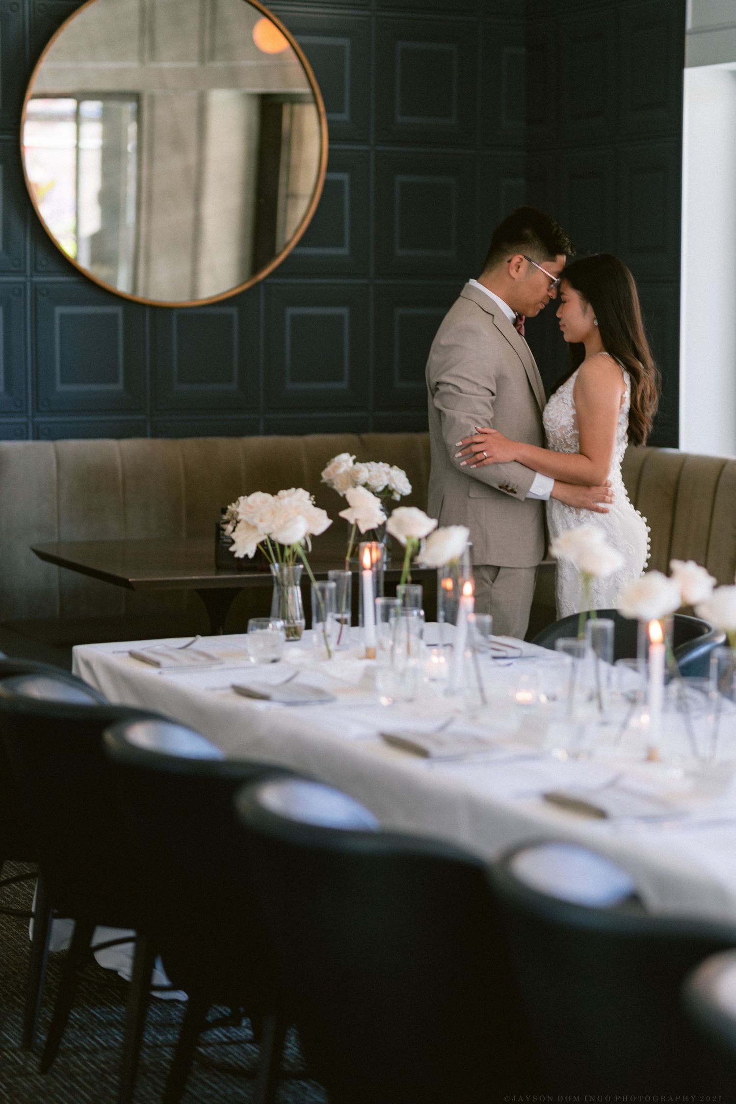 Romantic dining room setting with round mirror, blue walls, and elegant table decorated with white flowers and glassware.