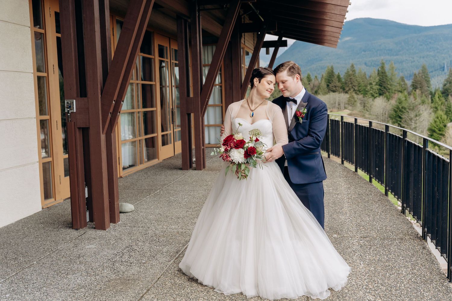 A romantic wedding couple poses on a scenic outdoor balcony with mountain views in the background.