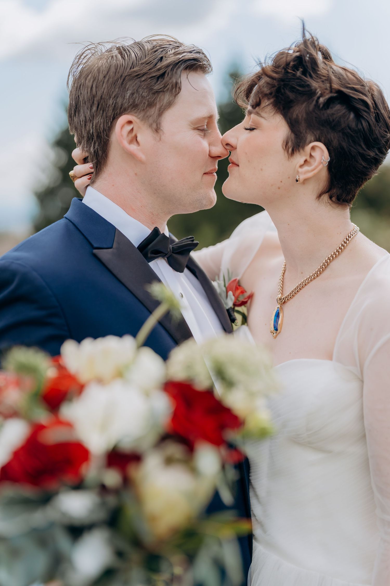 Close-up of romantic wedding couple sharing an intimate moment with red and white flowers in foreground.