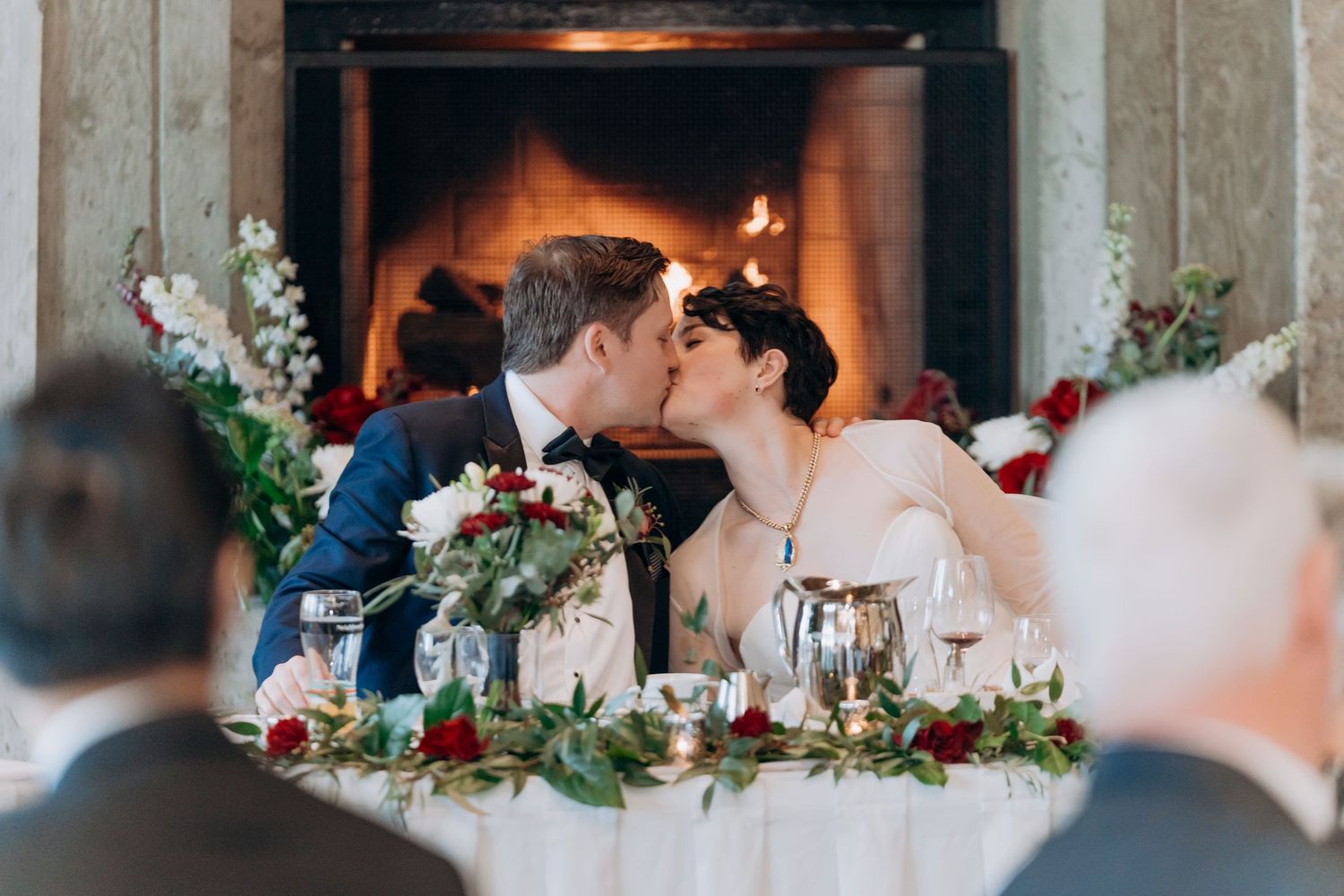 Cozy wedding reception venue with glowing fireplace and floral table decorations.