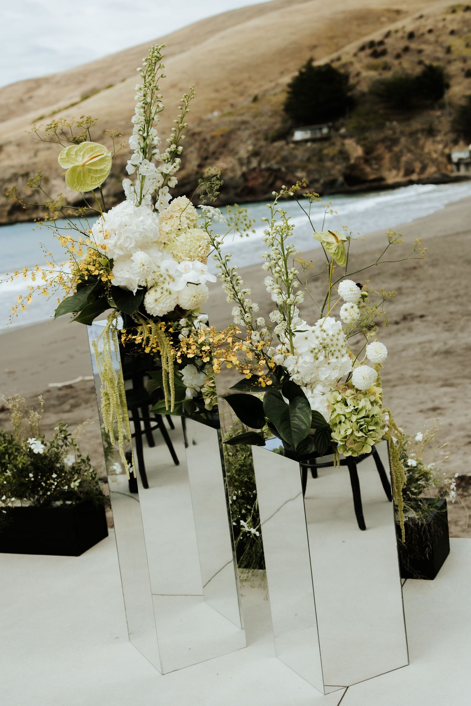 White floral arrangements in modern glass vases against coastal landscape.